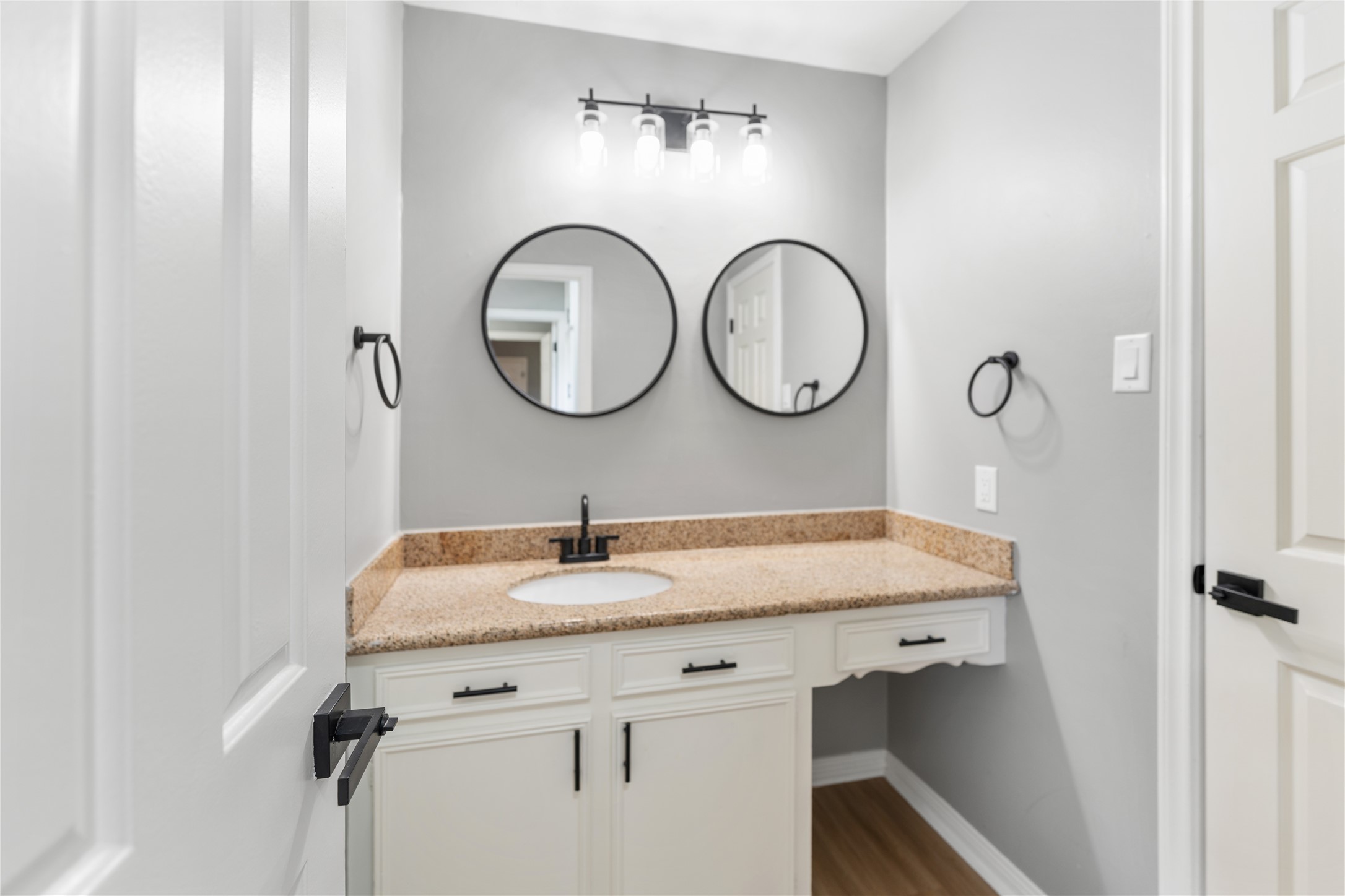 The secondary Jack and Jill style bathroom features a modern vanity with a granite countertop, dual round mirrors, and stylish lighting. The neutral color palette and sleek fixtures create a clean, contemporary look.