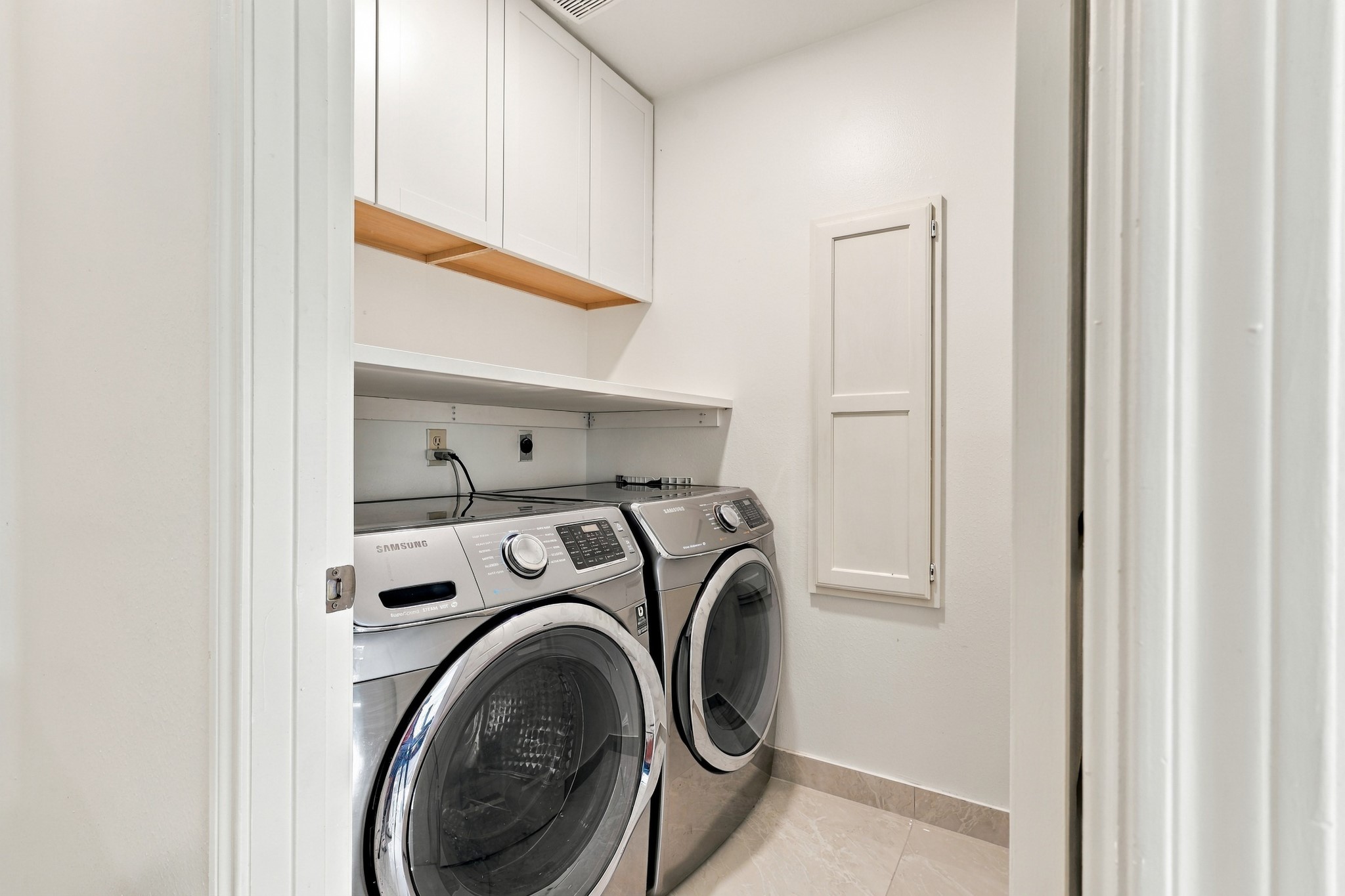 Convenient interior laundry room with full-size laundry capability, overhead cabinetry, and additional built-in storage. A dedicated folding counter and neutral tile flooring add functionality to this thoughtfully arranged utility space.