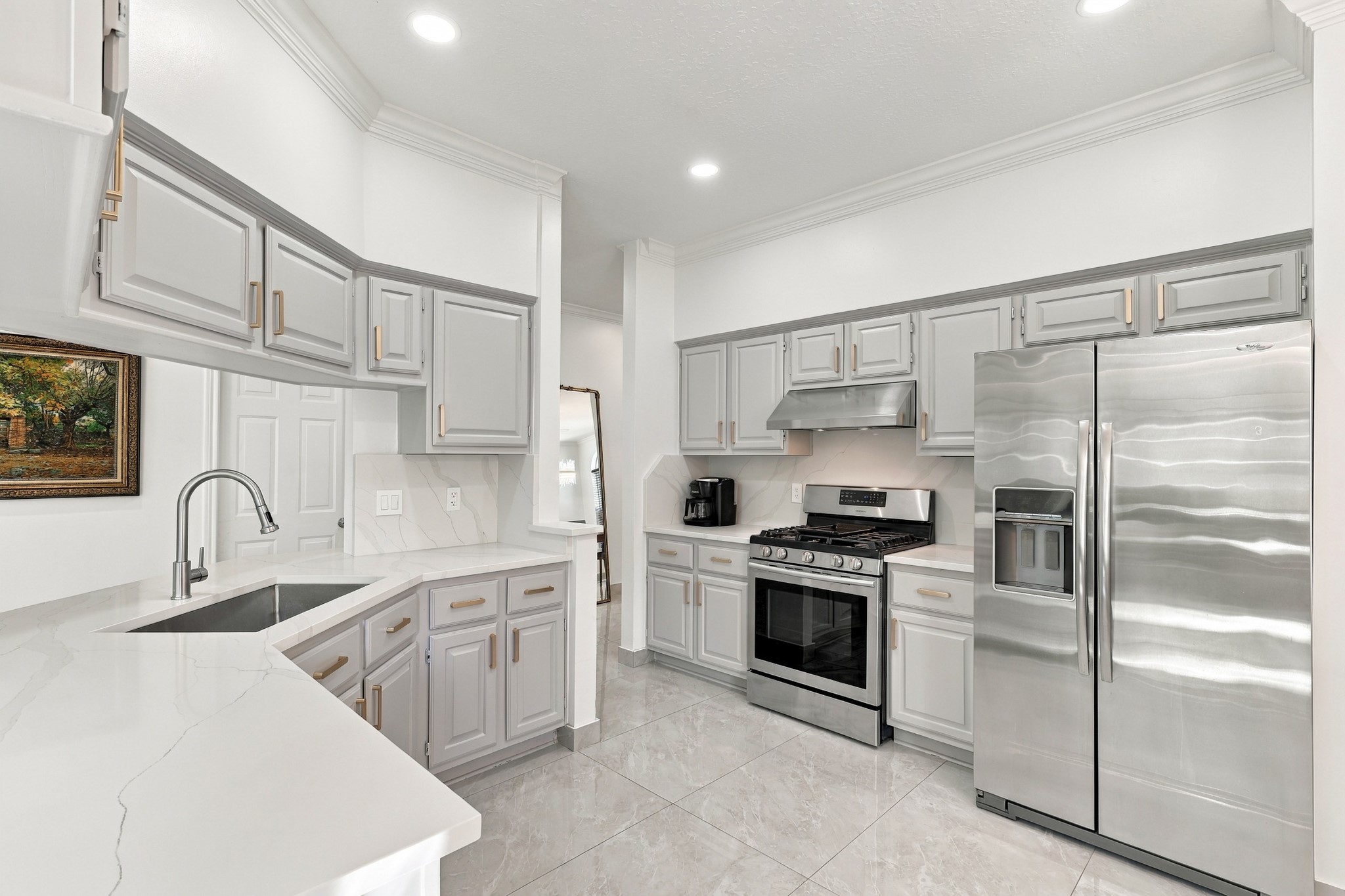 Beautifully appointed kitchen featuring abundant soft gray cabinetry with brushed gold hardware, white quartz-countertops, and coordinating marble backsplash. Stainless steel appliances, a gas range, undermount sink, recessed lighting, and generous counter space combine style and functionality, while the wraparound breakfast bar provides additional seating and serving space. Beautifully appointed kitchen featuring abundant soft gray cabinetry with brushed gold hardware, white quartz-countertops, and coordinating marble backsplash. Stainless steel appliances, a gas range, undermount sink, recessed lighting, and generous counter space combine style and functionality, while the wraparound breakfast bar provides additional seating and serving space.
