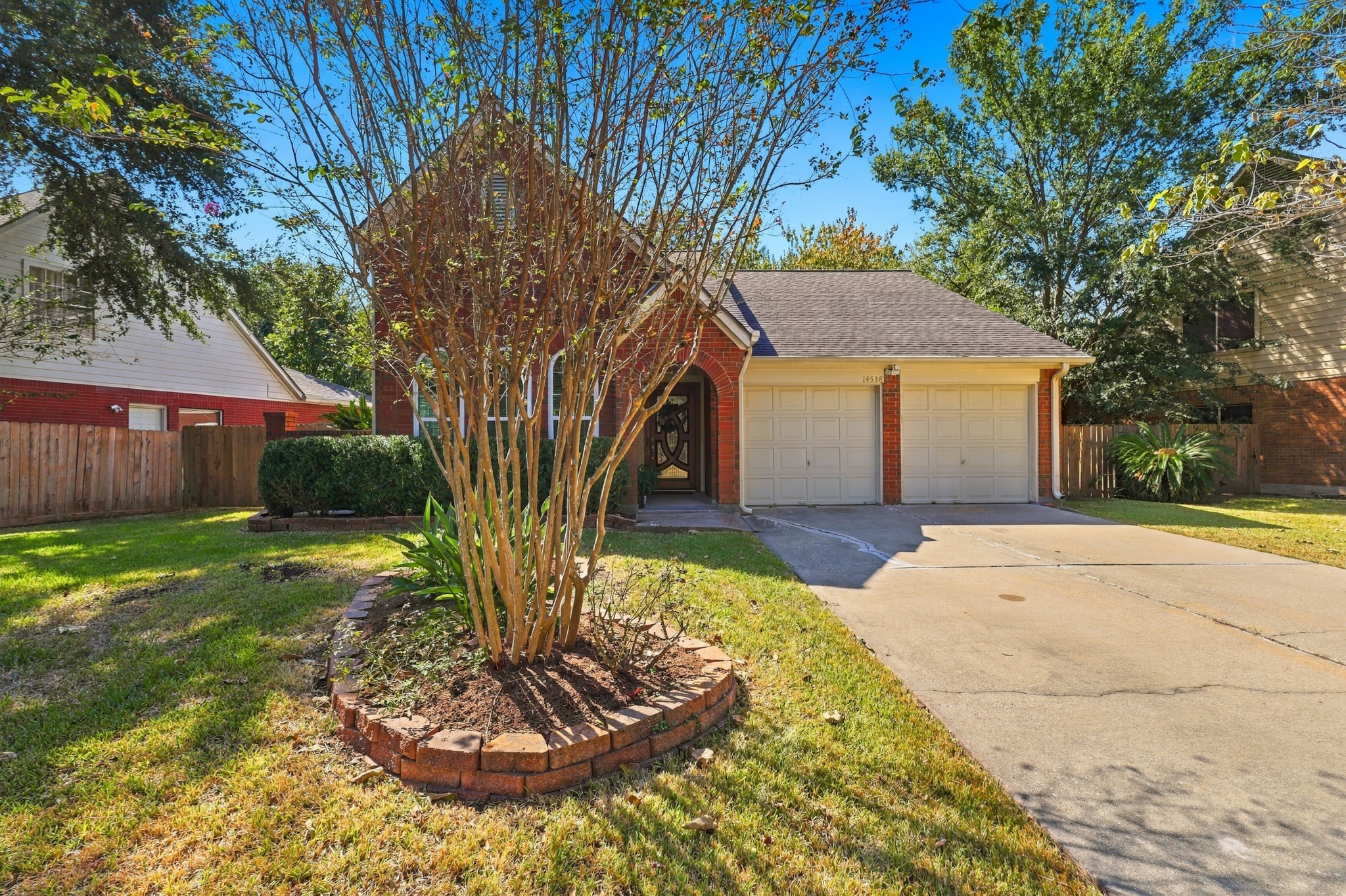 A closer look at the home's inviting curb appeal, featuring a charming arched entry with decorative front door, mature landscaping, brick-bordered planting beds, and a spacious driveway leading to the attached two-car garage. A closer look at the home's inviting curb appeal, featuring a charming arched entry with decorative front door, mature landscaping, brick-bordered planting beds, and a spacious driveway leading to the attached two-car garage.