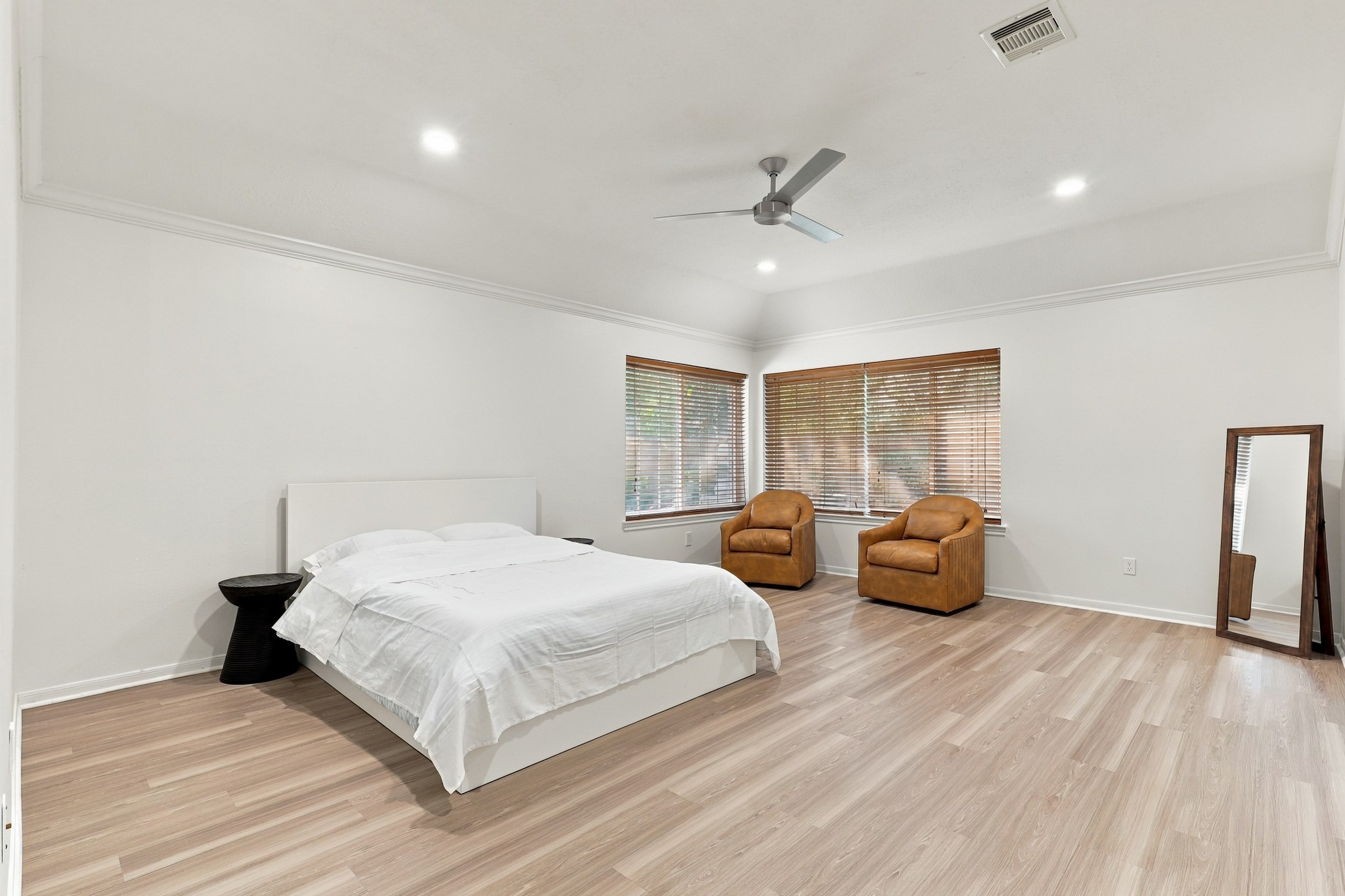 Expansive primary suite featuring beautiful wood flooring, crown molding, recessed lighting, and a modern ceiling fan. Two large windows fill the room with natural light, while the generous layout easily accommodates a sitting area or additional furnishings.