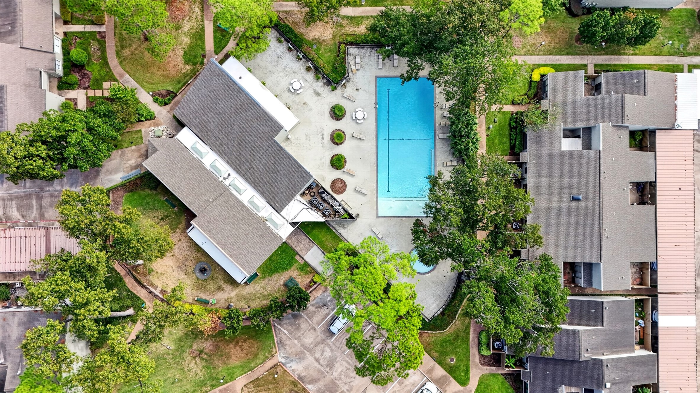 Top-down aerial of the community pool and clubhouse deck, lined with loungers and shaded by oaks.