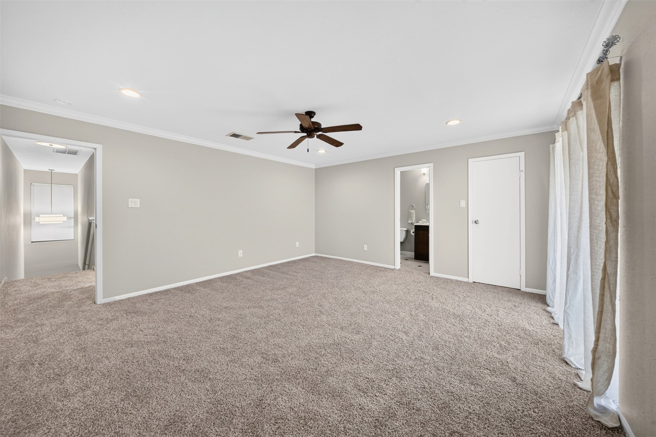 Another angle of the second bedroom: sheer-curtained windows, a ceiling fan, and doorways to the ensuite bath and closet.