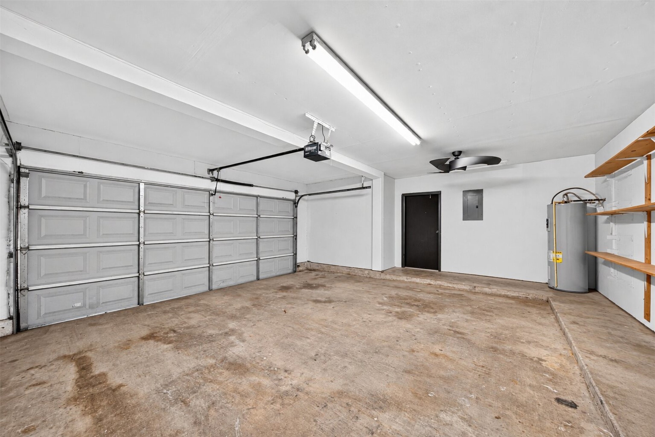 The oversized two-car garage features an automatic opener, built-in wood shelving, a ceiling fan, and room for the water heater plus storage.