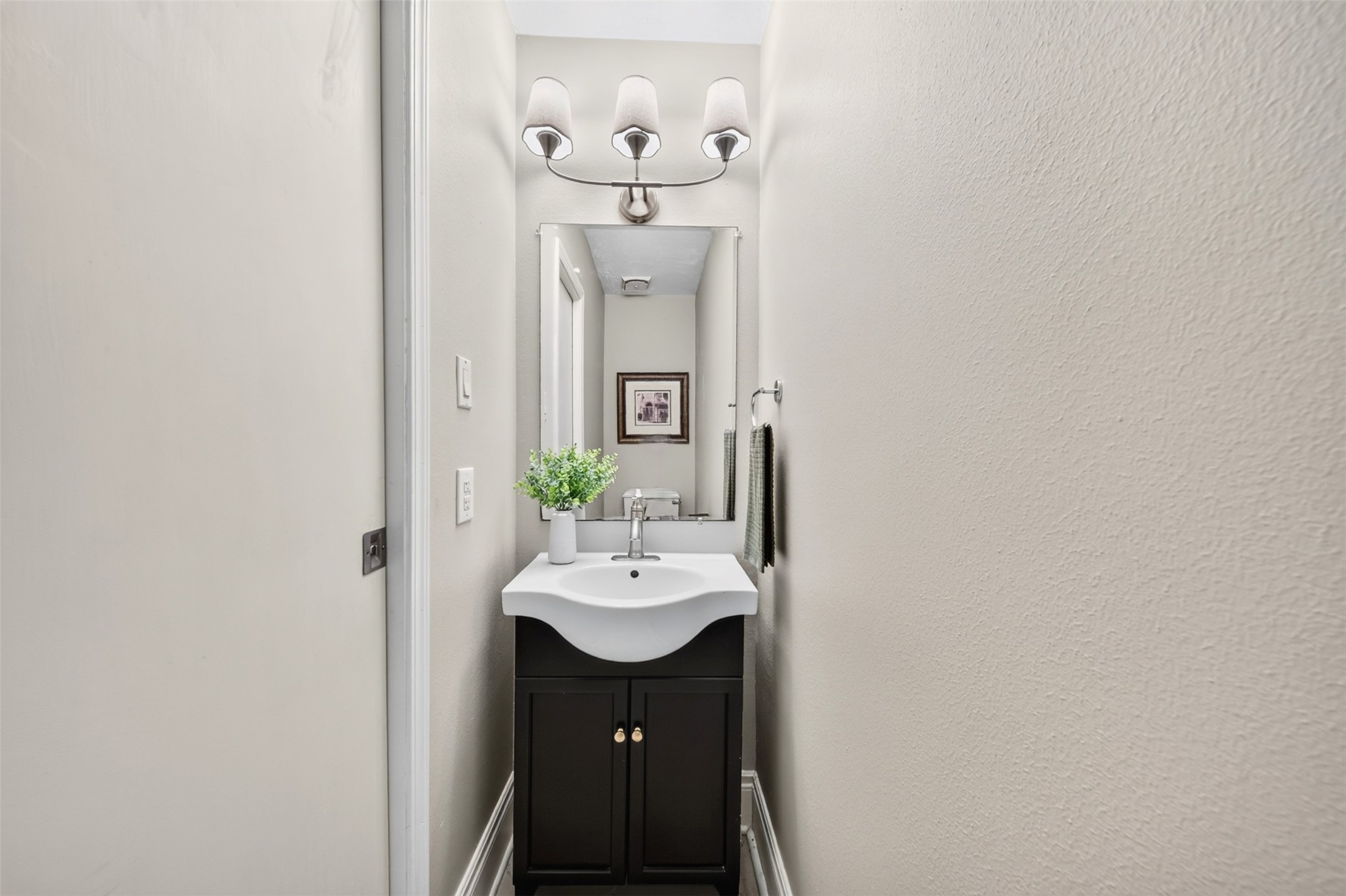 A tidy main-floor powder room with a dark vanity cabinet, scalloped white sink, mirrored medicine cabinet, and a three-light fixture  convenient for guests.