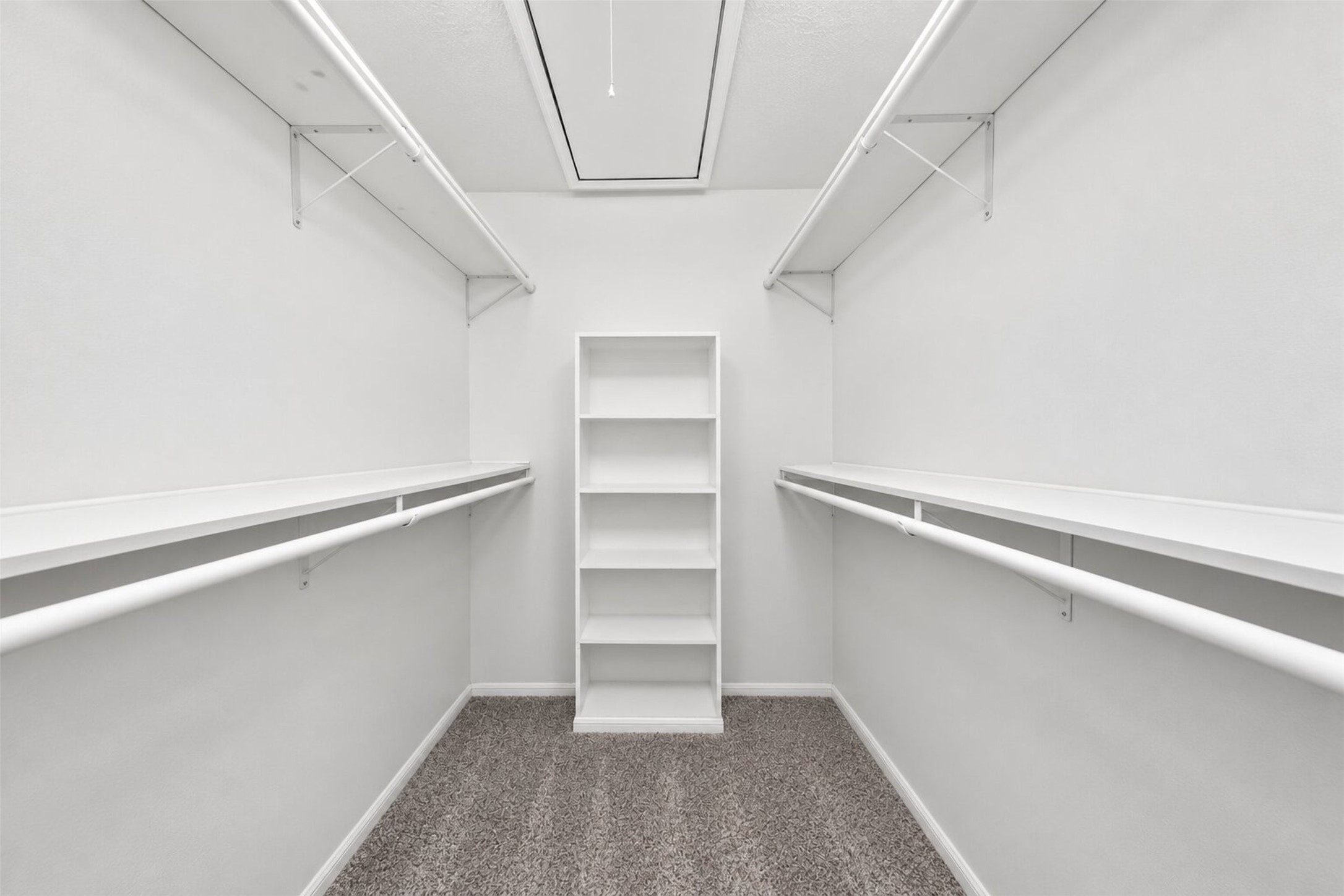 The primary walk-in closet is lined with double hanging rods and shelving on both sides, plus a built-in shelving tower and attic access above.