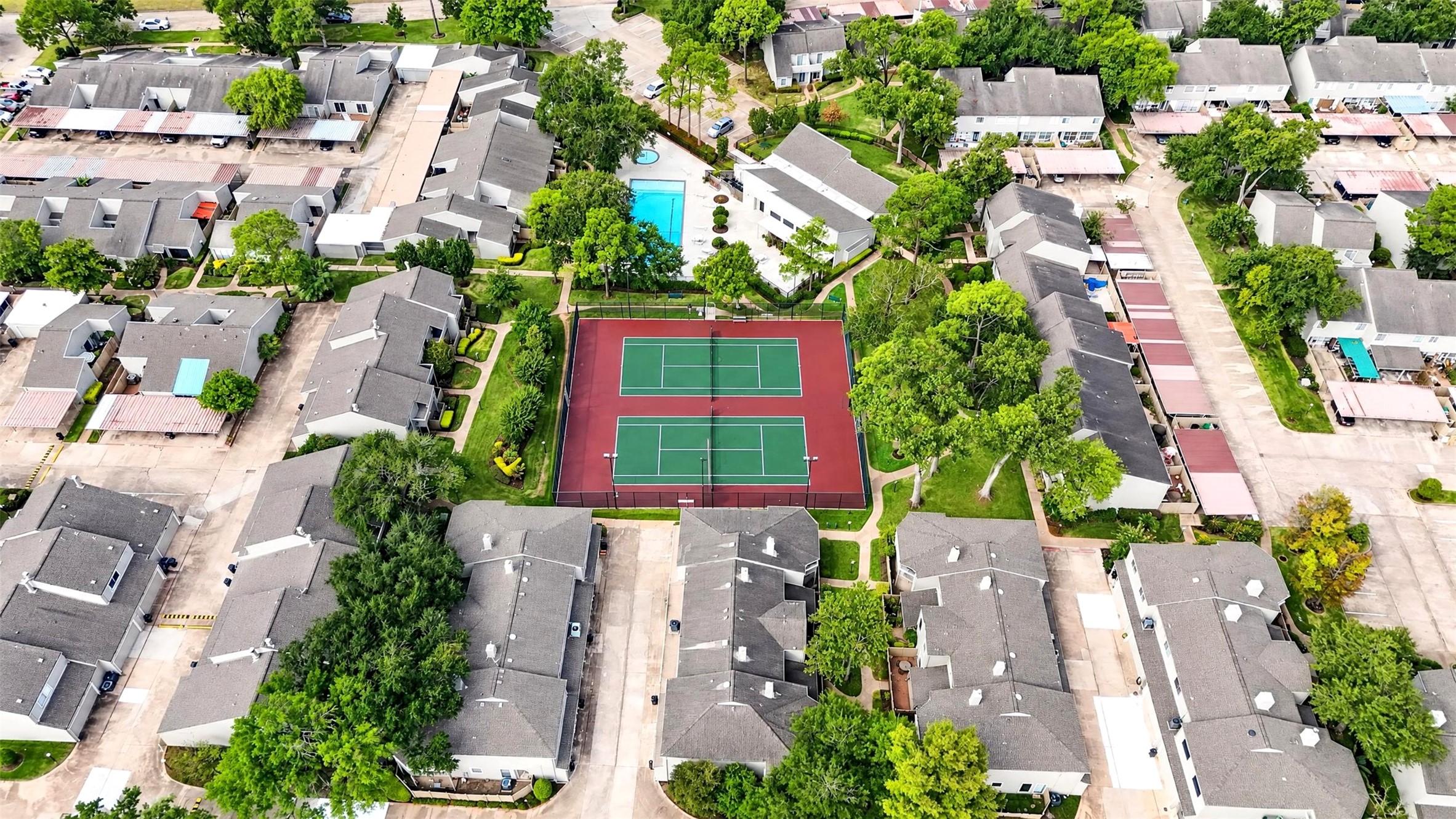 Aerial view over the community's two tennis courts and pool, surrounded by townhome rooftops and mature trees.