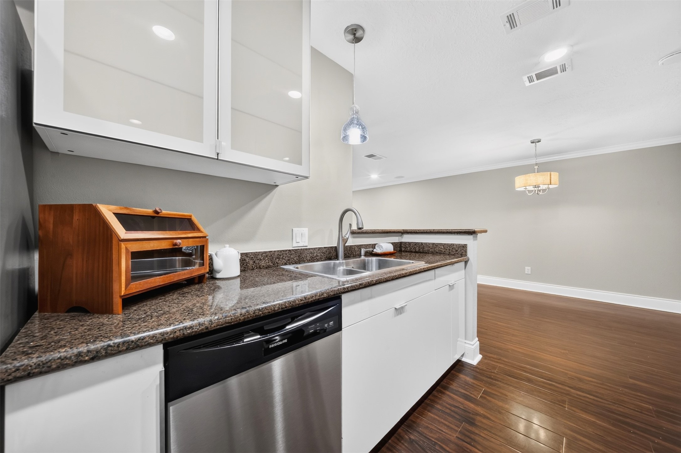 Along the sink counter: a stainless double sink, dishwasher, and a pendant light above, with the dining room and its chandelier open beyond the breakfast bar.