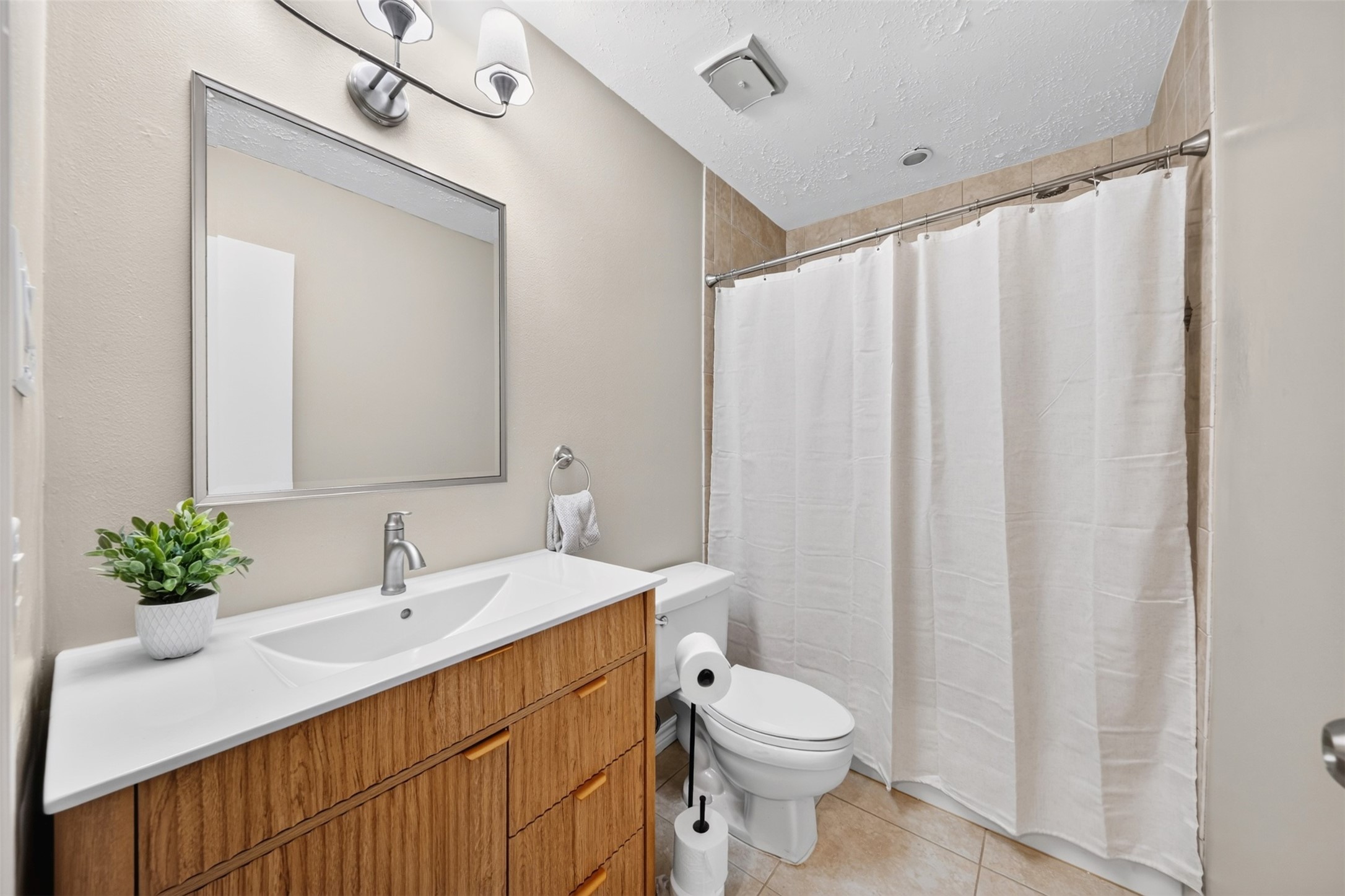 The primary bath features a wood-front vanity with an integrated sink, a large framed mirror, and a tub/shower combo with tile surround. Tile floors and brushed-nickel fixtures.
