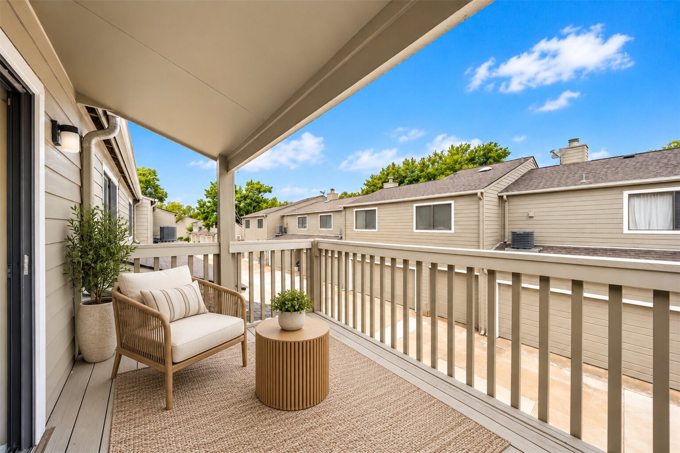 Virtually staged with a woven lounge chair and side table, the covered upstairs balcony becomes a private perch for morning coffee, overlooking the quiet community below.