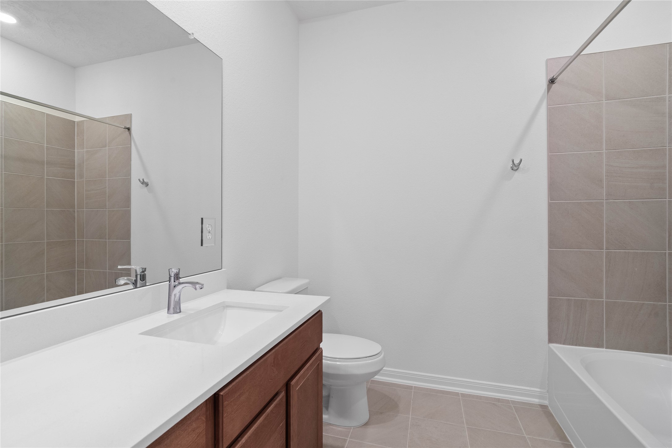 Well-appointed secondary bath with tub/shower combination and tile surround. It also features an extended vanity with a light countertop and a mirror that extends the full length of the vanity.