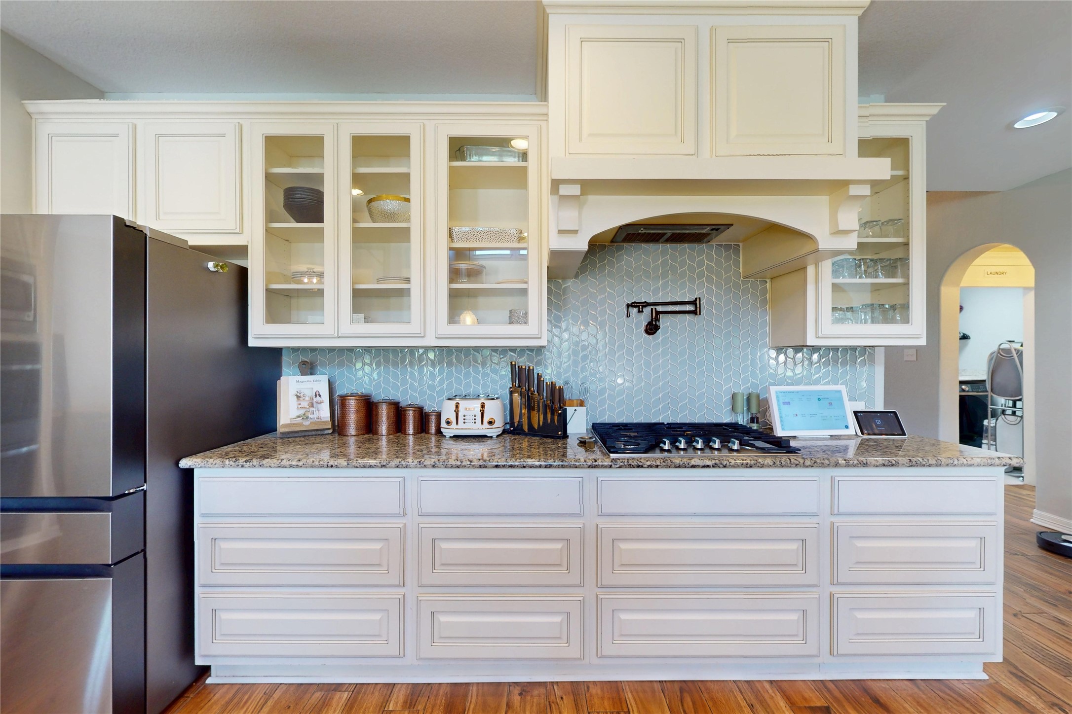 Gas cooktop with glass tile backsplash and glass-front cabinetry