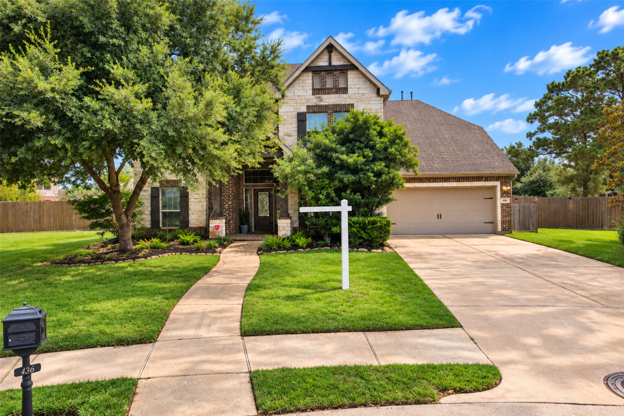Brick and stone elevation with mature trees and wide driveway