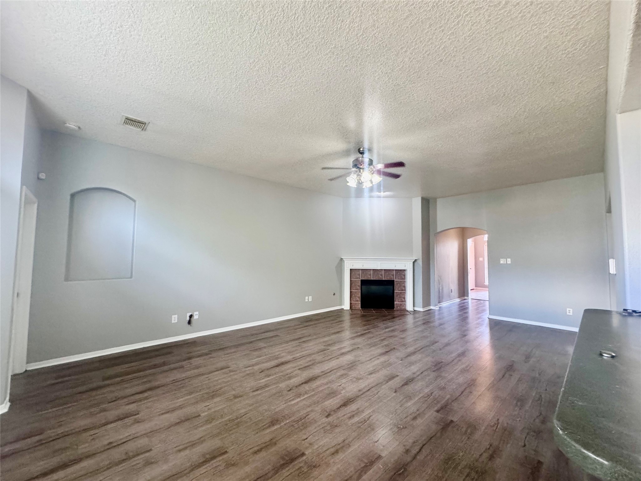 Spacious living area with elegant wood flooring, a cozy fireplace, and a ceiling fan, perfect for comfortable living and entertaining.