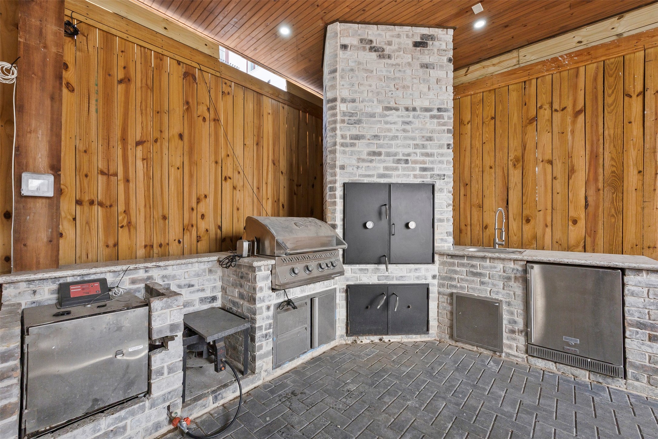 Covered outdoor kitchen with built-in grill, generous prep space, stone finishes, and wood ceiling, extending the home's entertaining capabilities outdoors.