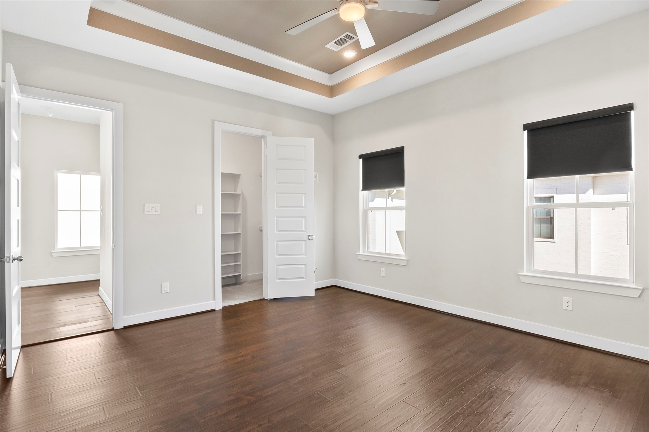 Alternate view of the spacious primary suite showcasing tray ceilings, abundant windows, and flexible furniture placement options.