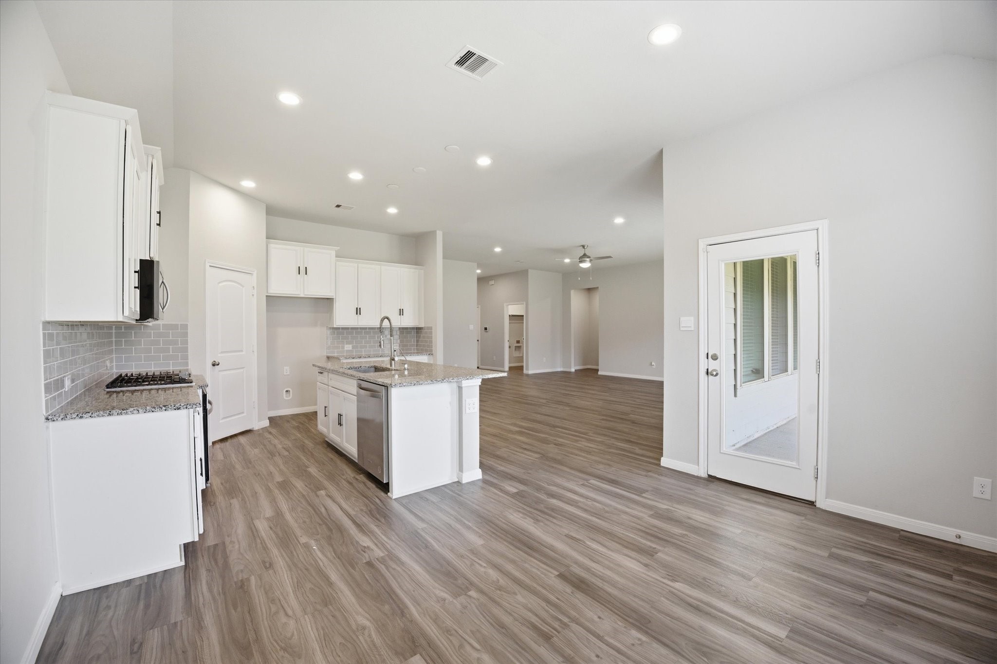 This bathroom features a modern design with a double vanity, large mirror, and sleek fixtures. It has a bathtub with gray tile surround and wood-style flooring, providing a clean and contemporary aesthetic.