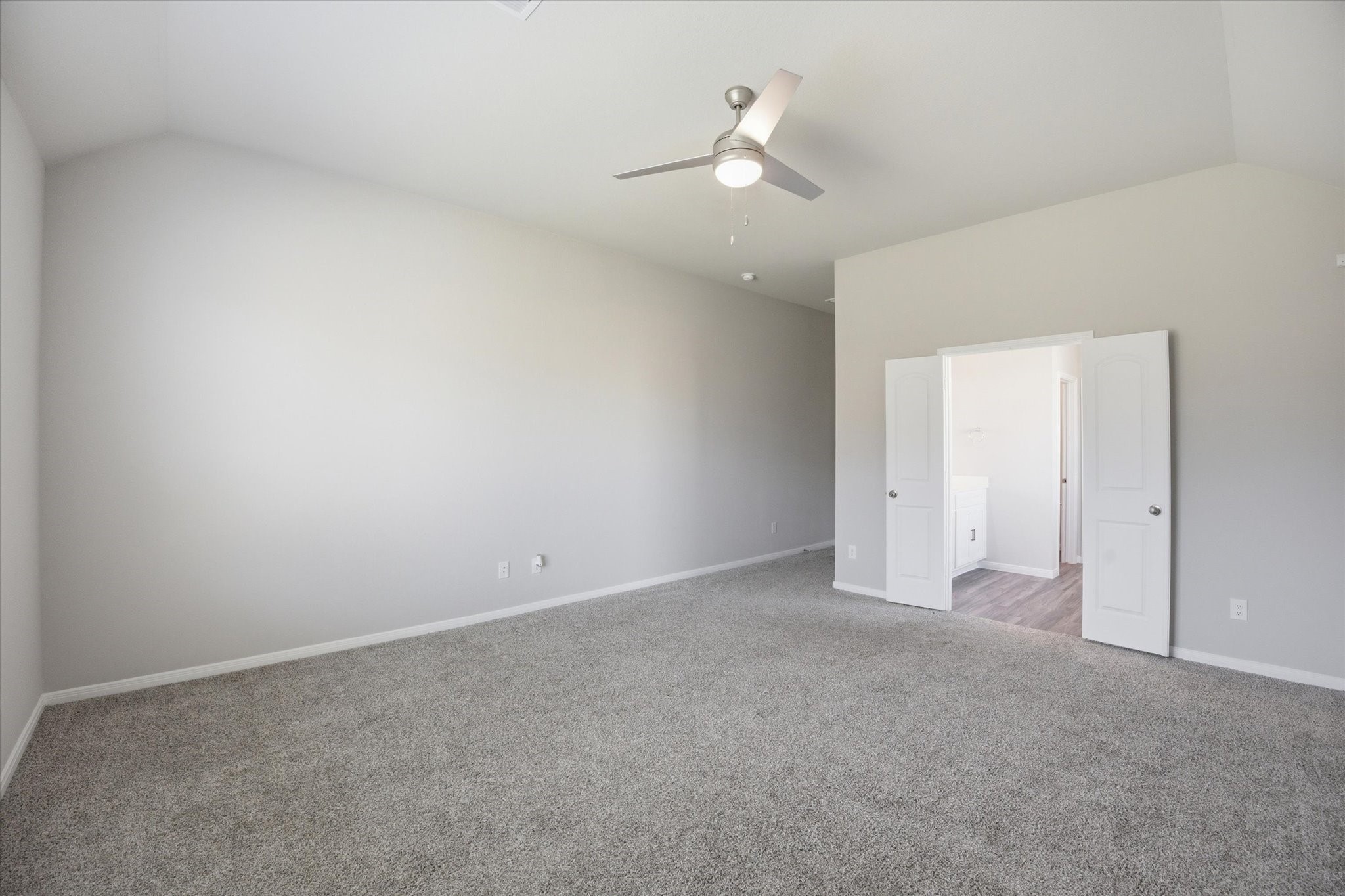 This spacious master bedroom features plush carpeting, a modern ceiling fan, and an inviting entrance to an en-suite bathroom, offering a perfect blend of comfort and style.