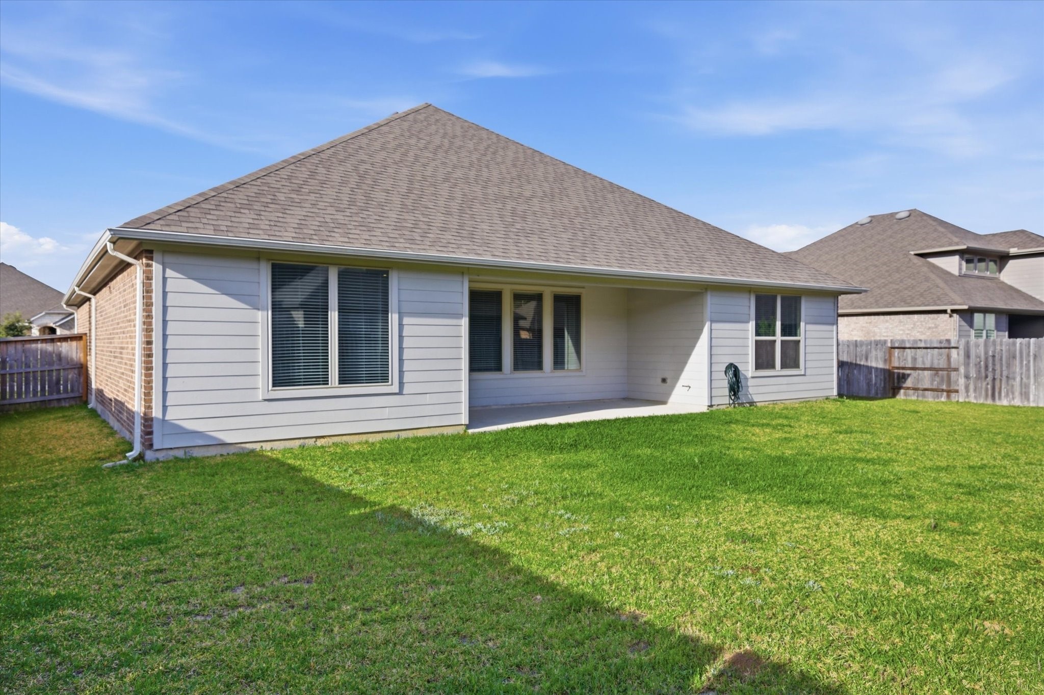 This photo shows the backyard of a single-story home with a spacious lawn, a covered patio, and a fenced boundary, perfect for outdoor activities and privacy.