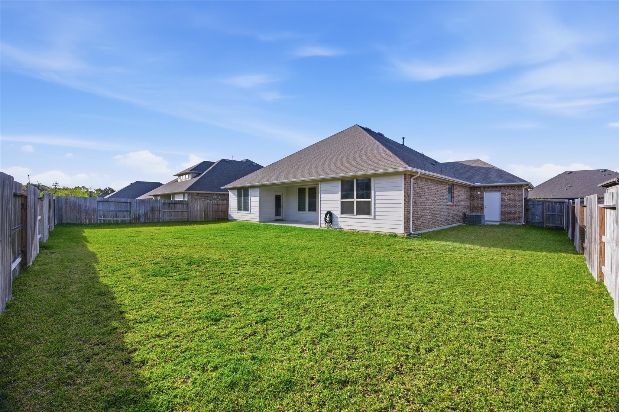 A spacious, fenced backyard with a well-maintained lawn and a modern, single-story brick house featuring large windows. Ideal for outdoor activities and privacy.