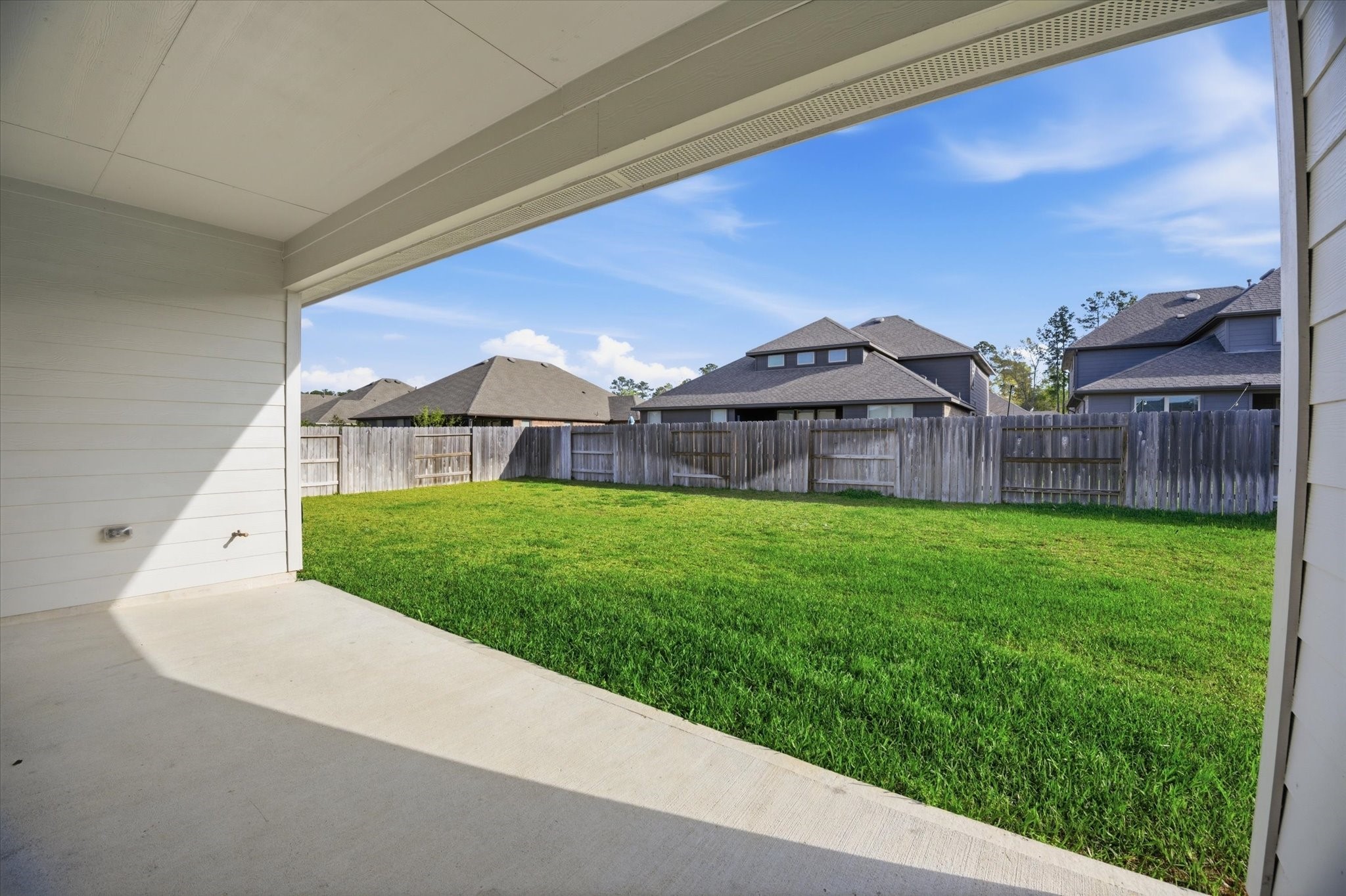 This photo shows a covered patio opening to a spacious, fenced backyard with a well-maintained lawn, ideal for outdoor activities and privacy.