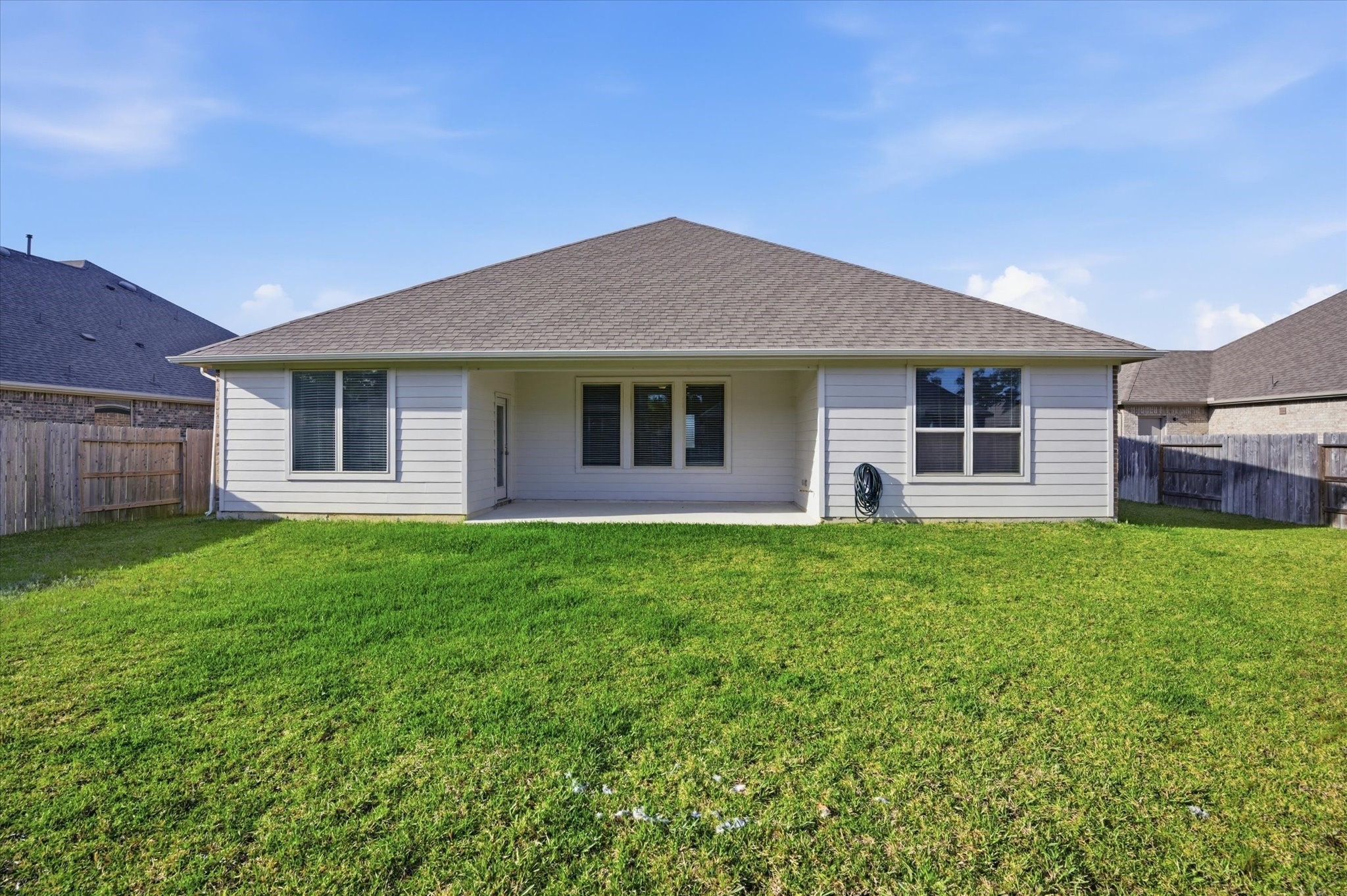 This photo shows the back of a single-story home with a spacious, well-maintained lawn. The house features a covered patio area, a sloped roof, and is surrounded by a wooden fence, offering privacy and outdoor space.