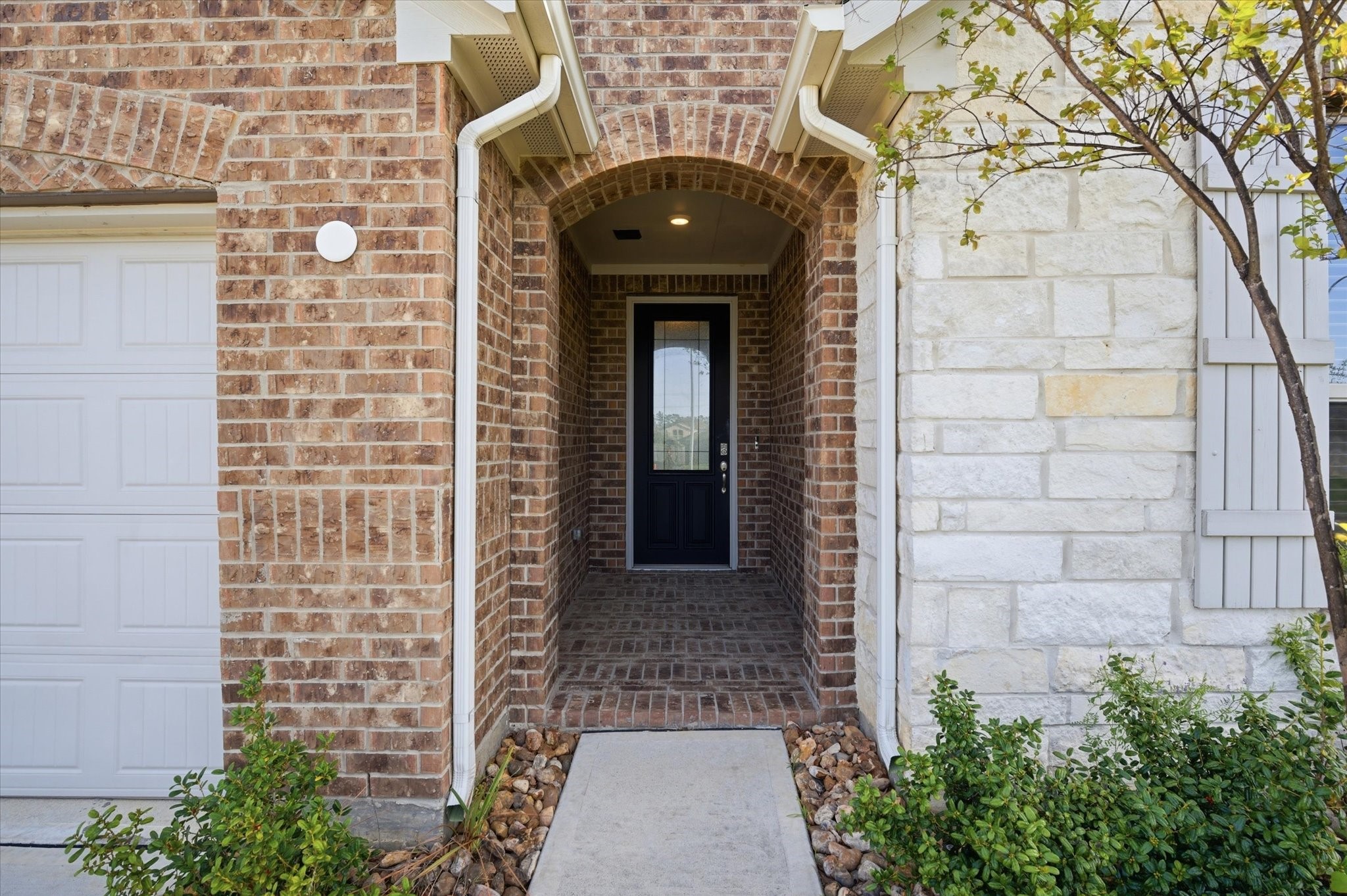 This photo shows a welcoming entryway with a dark front door featuring glass panels, neutral walls, and wood flooring. It has a modern, clean look with a small wall decoration and a door leading to another room.