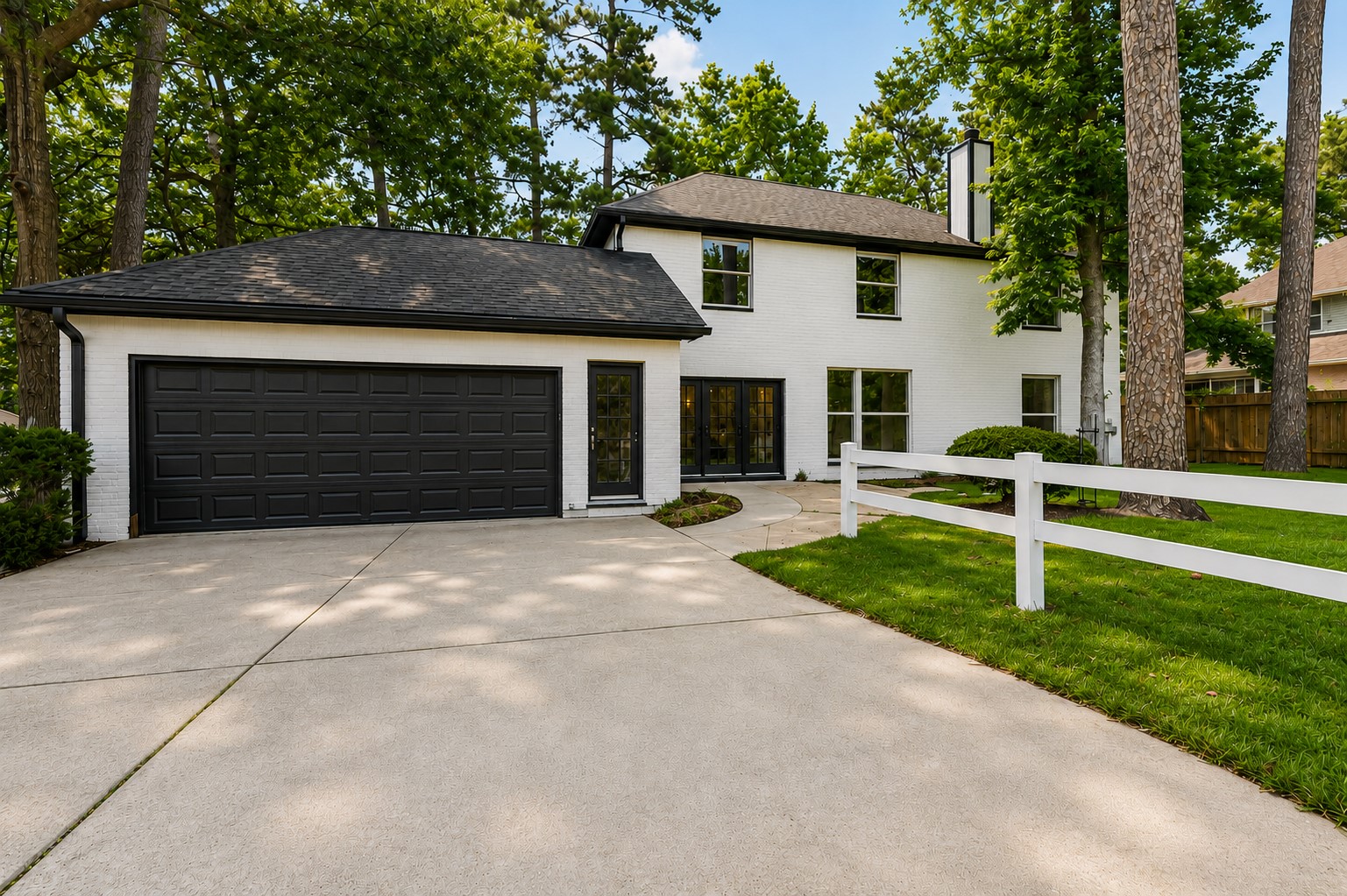Charming two-story home with a sleek black and white exterior, featuring a spacious driveway leading to a two-car garage, all set amidst a beautifully landscaped, tree-lined yard. Photo digitally enhanced.