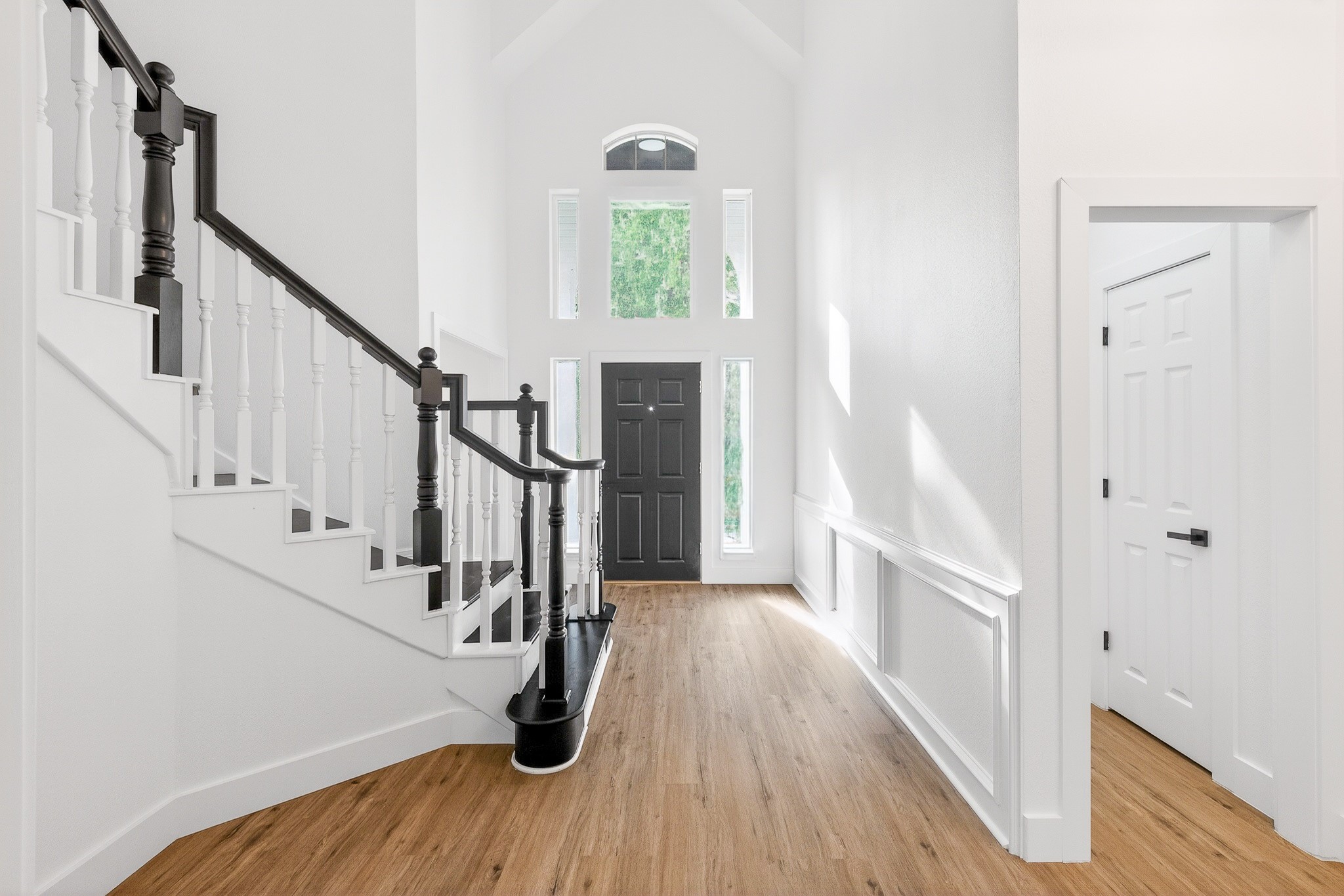 Bright and inviting foyer with high ceilings, elegant staircase, and beautiful luxury vinyl flooring leading to a striking black front door.