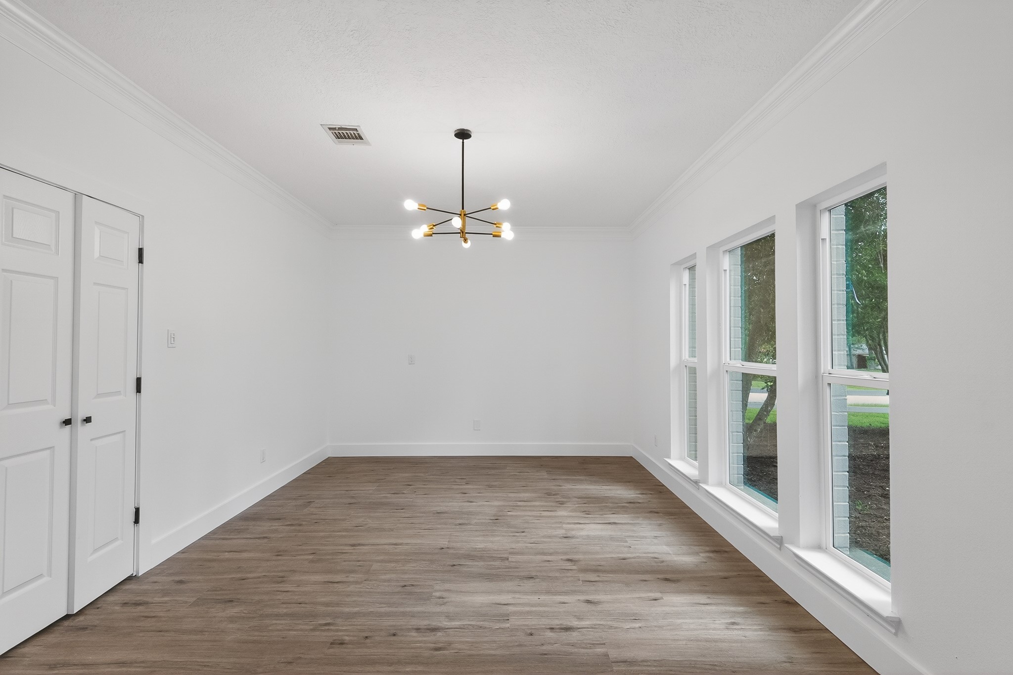 Bright and inviting room with large windows, sleek luxury vinyl flooring, and a modern chandelier, perfect for a dining area or living space.