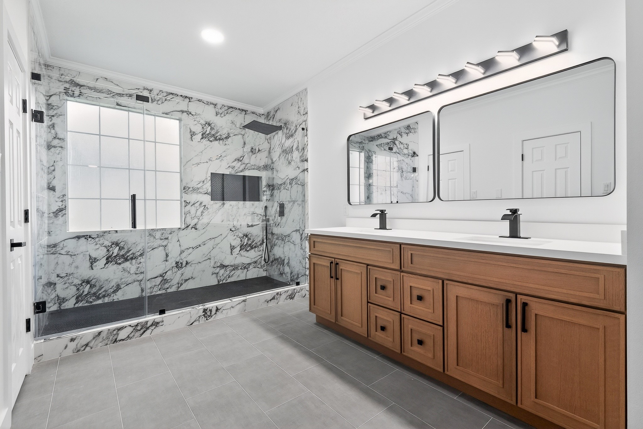 Elegant bathroom featuring a spacious walk-in shower with marble-style walls, dual sinks with modern fixtures, and ample wooden cabinetry for storage.
