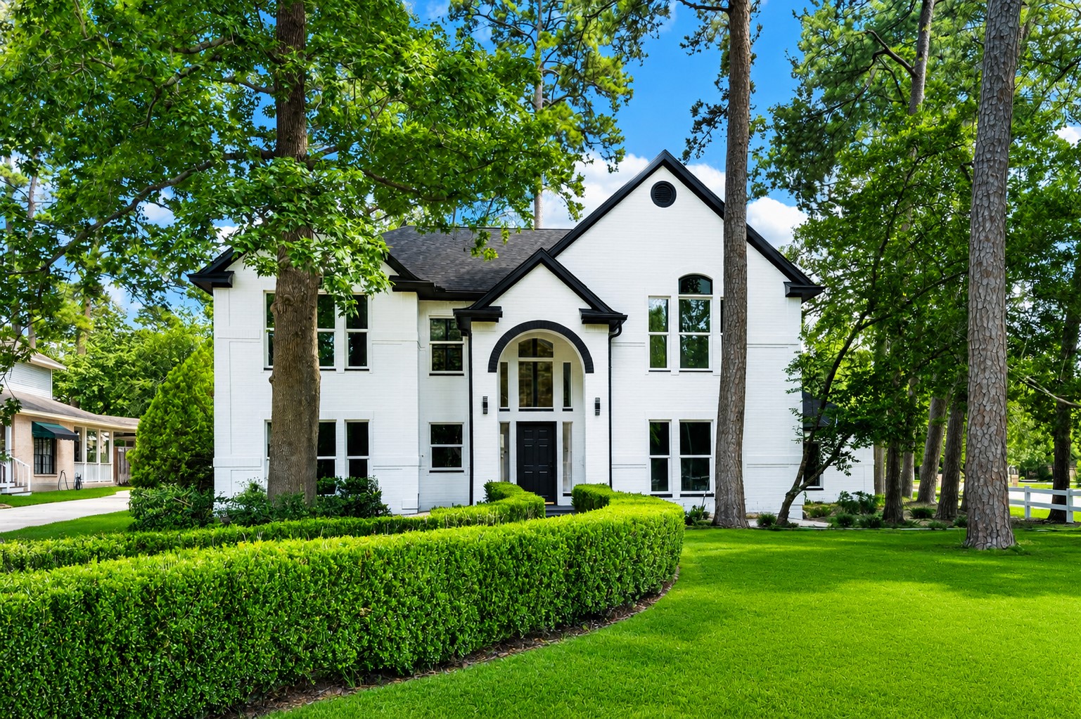 *Photo Digitally enhanced.
Elegant two-story home with a striking white brick exterior, nestled among mature trees and lush greenery, featuring arched windows and a welcoming entryway.