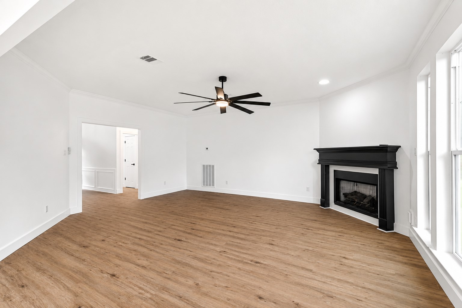 Spacious living room with elegant luxury vinyl flooring, a sleek black fireplace, and abundant natural light streaming through large windows.
