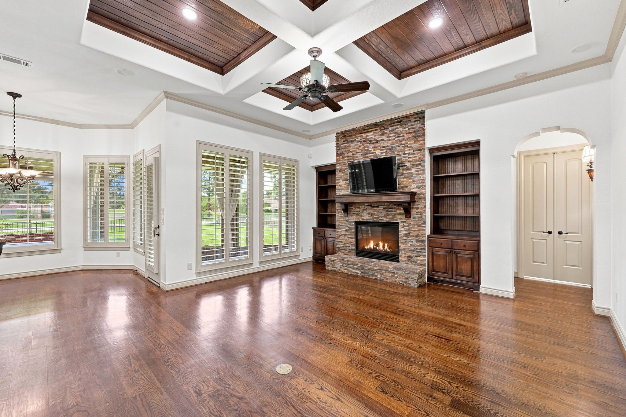 The spectacular Family Room is designed for both elegant entertaining and comfortable everyday living. A beautifully crafted wood coffered ceiling adds warmth and architectural distinction, while an impressive gas-log Fireplace is framed by a striking stacked-stone surround and custom built-in shelving on either side. Rich wood floors extend throughout the space, while numerous windows with Plantation Shutters fill the room with natural light and offer picturesque views of the gorgeous backyard.