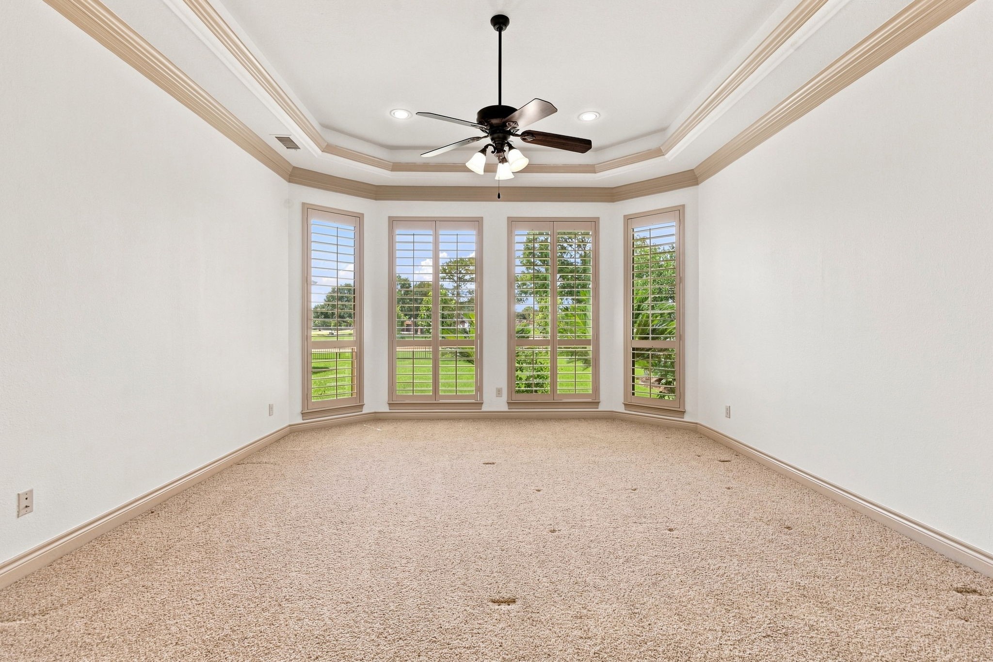 The expansive Primary Bedroom offers a luxurious and serene retreat, featuring lush wall-to-wall carpeting and a dramatic raised ceiling accented by elegant crown molding. Four large windows with Plantation Shutters fill the room with natural light while providing beautiful views of the gorgeous backyard.