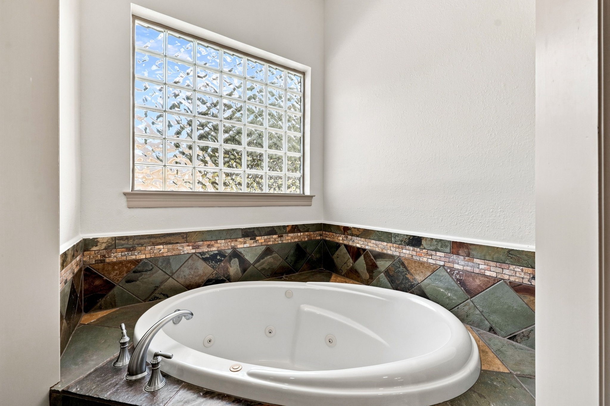 The luxurious jetted tub is perfectly positioned beneath a wall of elegant block-glass windows, allowing natural light to filter into the space while maintaining privacy. A beautiful slate-tile surround completes the sophisticated look, creating a relaxing focal point within the Primary Bathroom.