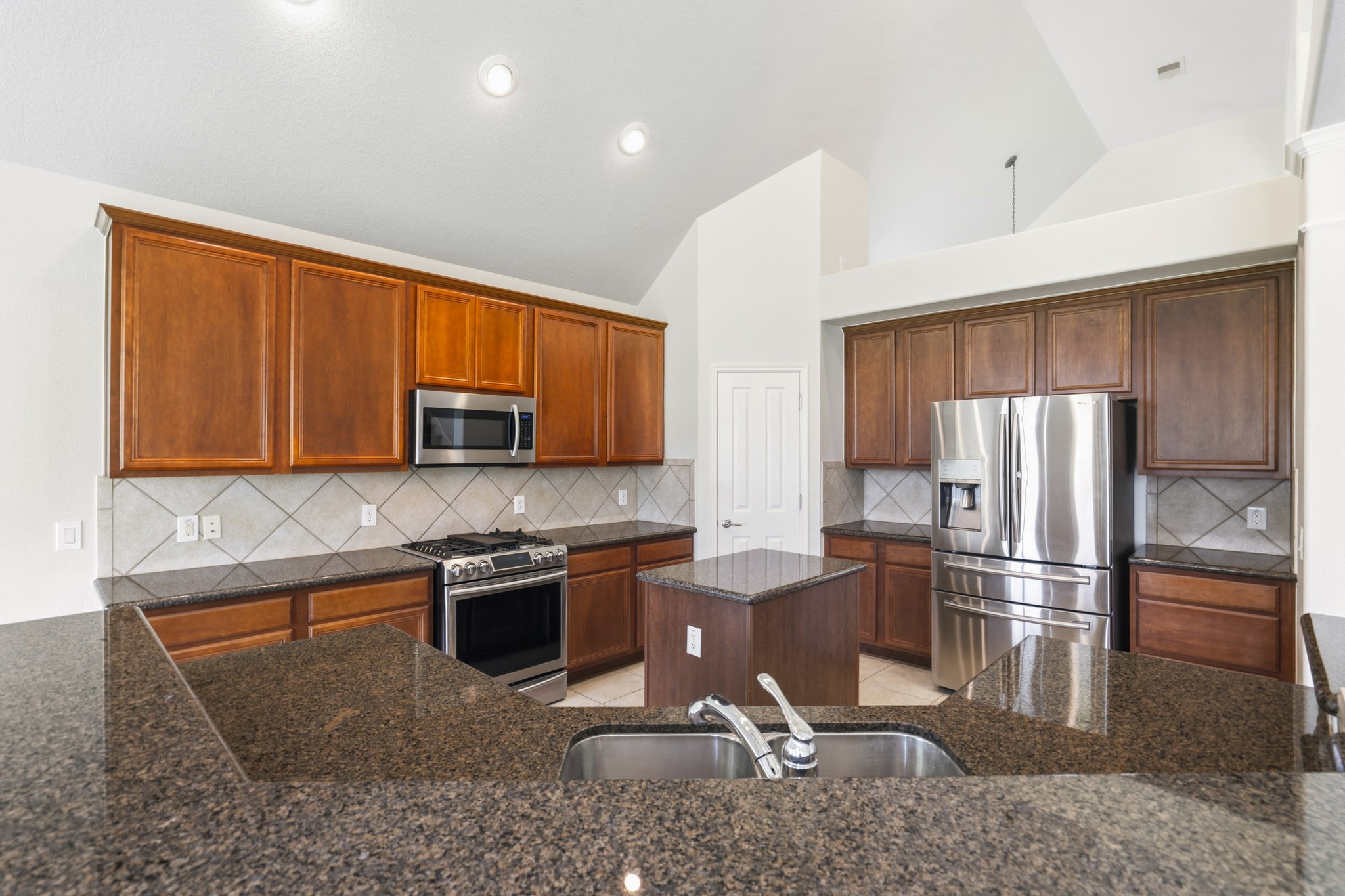 Chef-inspired kitchen featuring gleaming granite countertops, stainless steel appliances, a walk-in pantry, a five-burner gas cooktop with grill, center island, and included refrigerator.
