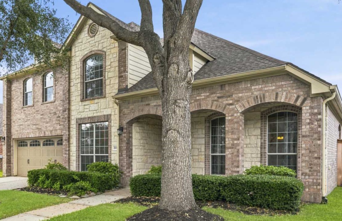 Front elevation featuring mature oak trees, lush landscaping, and the home's recently installed roof.