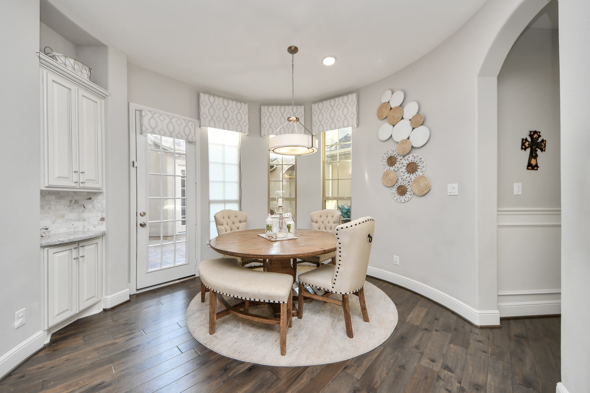 Inviting breakfast area featuring a convenient coffee bar, remote-controlled window coverings, and direct courtyard access. Adjacent hallway leads to the mudroom, utility room, rear staircase, and garages.