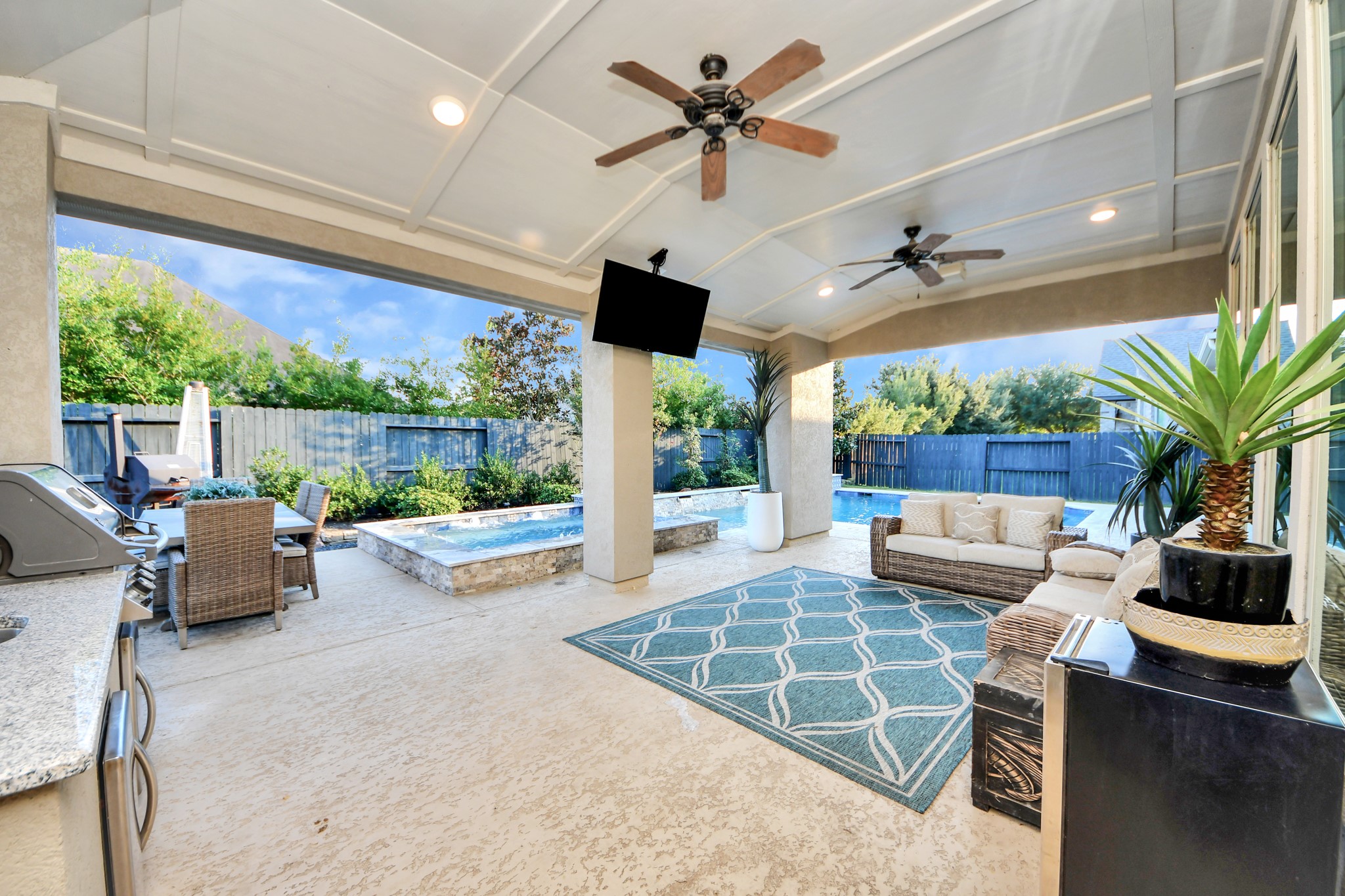 Expansive covered outdoor patio featuring stamped concrete, built-in speakers, two ceiling fans, mounted TV, and a fully equipped outdoor kitchen. Overlooking the oversized pool and spa, this private backyard oasis offers outdoor dining, mature landscaping, and exceptional privacy.