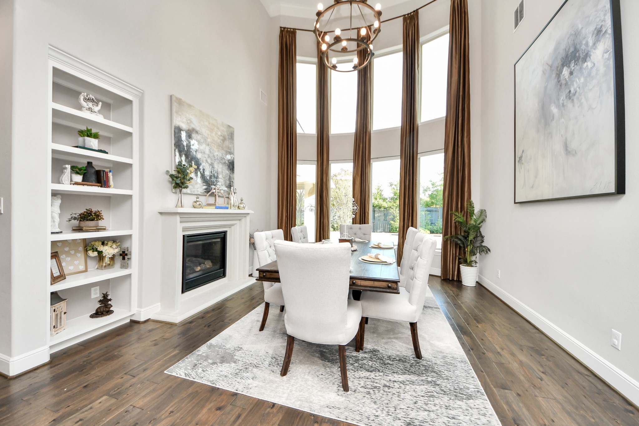 Elegant formal dining room featuring dramatic 20-foot ceilings, a double-sided fireplace, and expansive windows that fill the space with natural light.