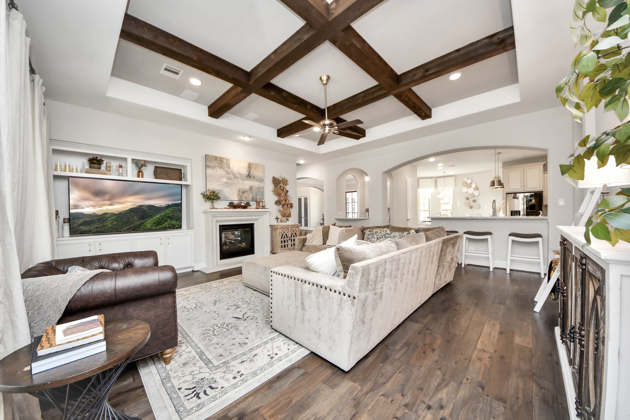 Spacious family room featuring a coffered-style ceiling accented by exposed wood beams, elegant arched openings, built-in surround sound speakers, and a stunning double-sided fireplace.