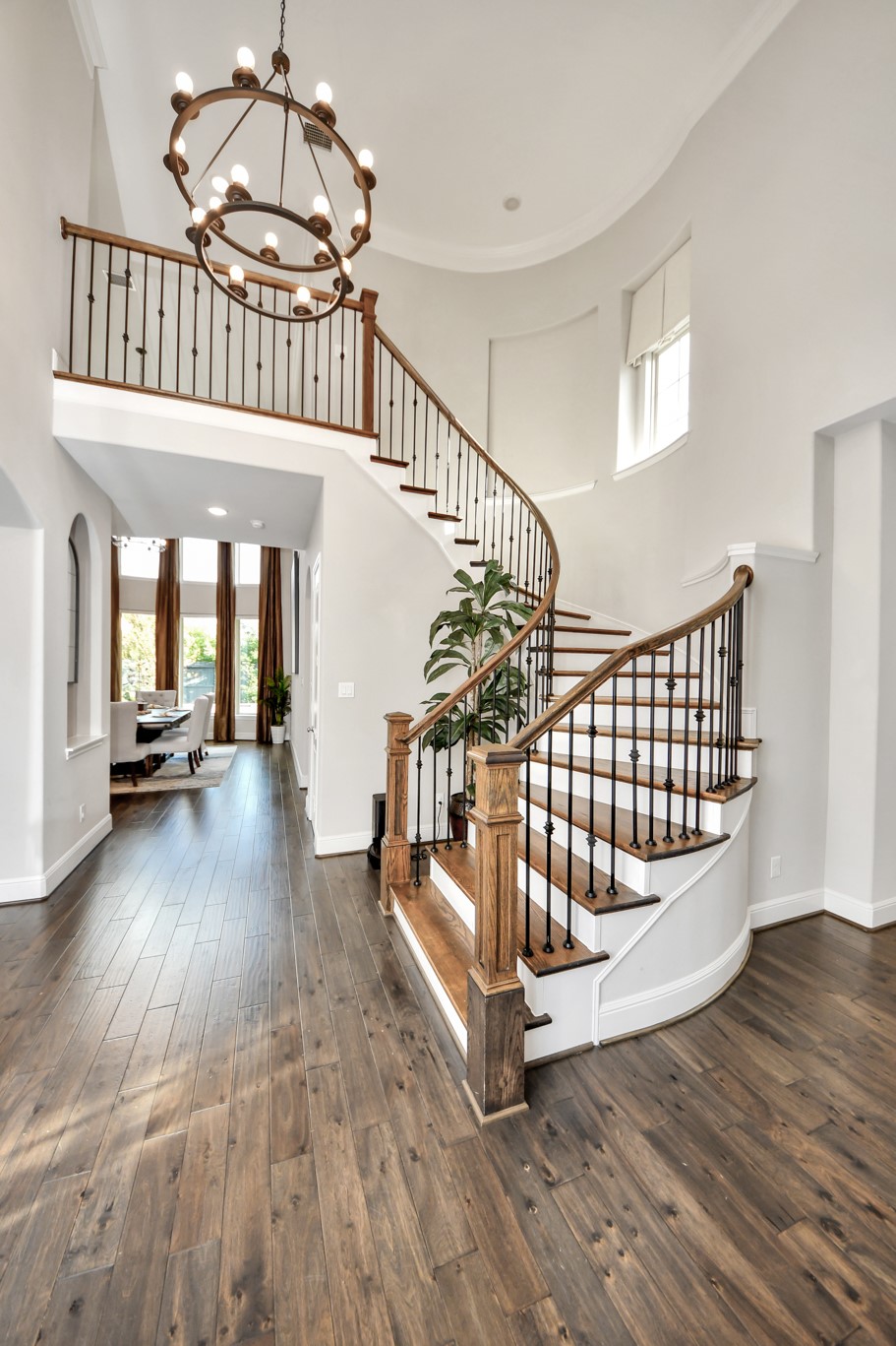 Grand entry featuring a stunning spiral staircase, statement chandelier, rich hardwood floors, and dramatic 20-foot ceilings, all beautifully illuminated by abundant natural light.