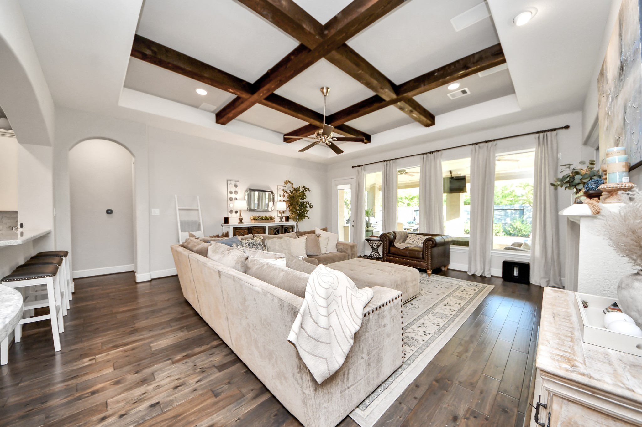 Spacious family room featuring a coffered-style ceiling with exposed wood beams, built-in surround sound speakers, and remote-controlled automatic window coverings.