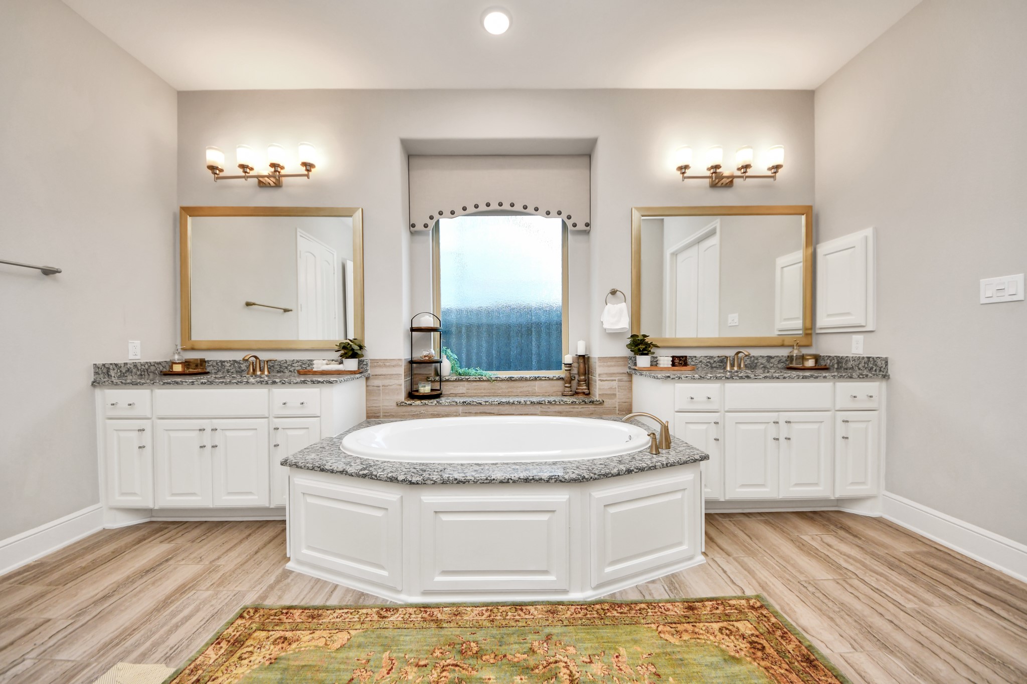 Spacious primary bathroom featuring a stunning 6-foot soaking tub, separate vanities with granite countertops, custom cabinetry, and an open, luxurious layout.