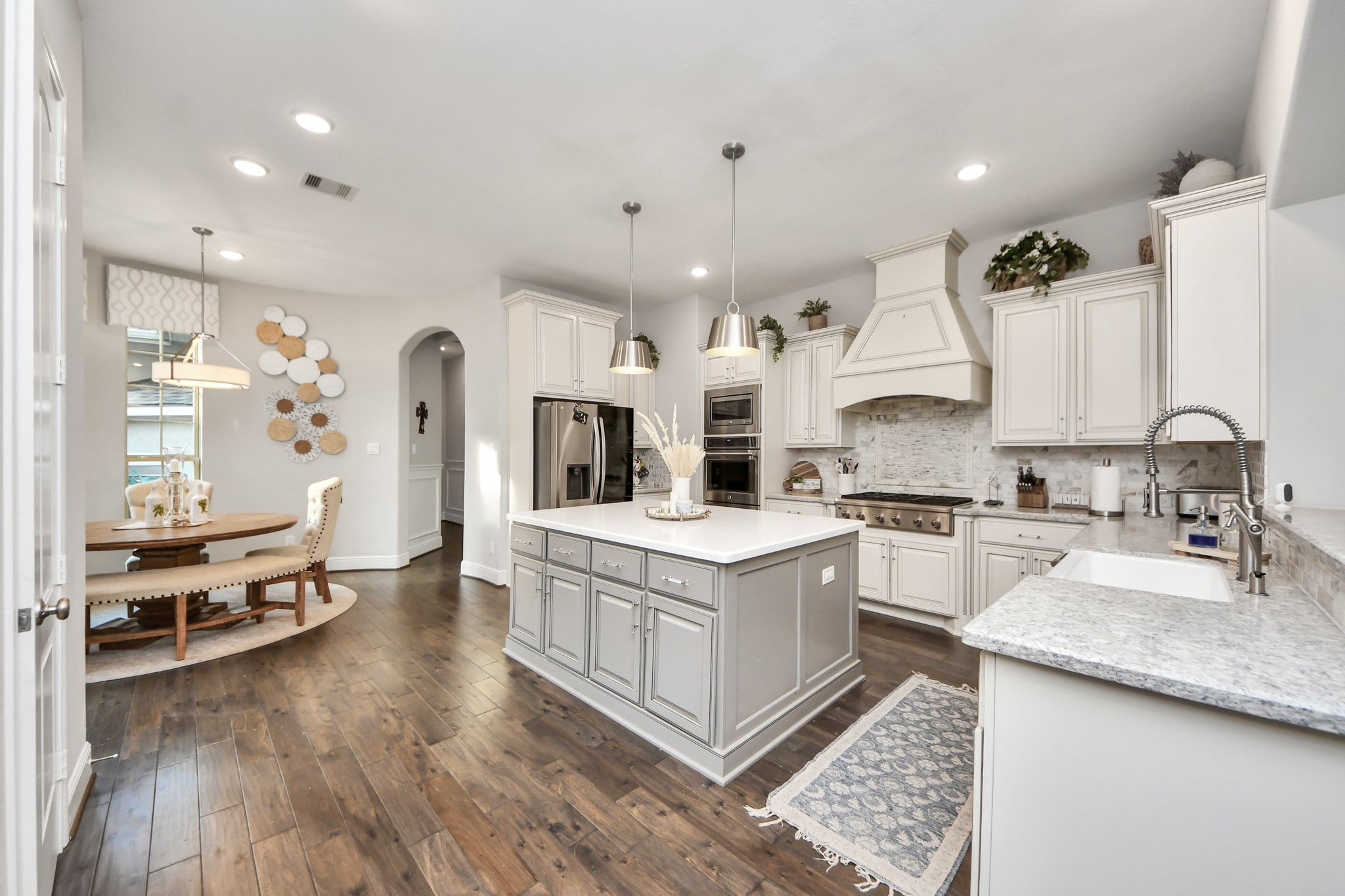 Gourmet kitchen featuring quartz countertops, a spacious center island, double ovens, six-burner cooktop, custom built-in vent hood, stainless steel appliances, and lower cabinetry equipped with custom pullout drawers and organizational storage.