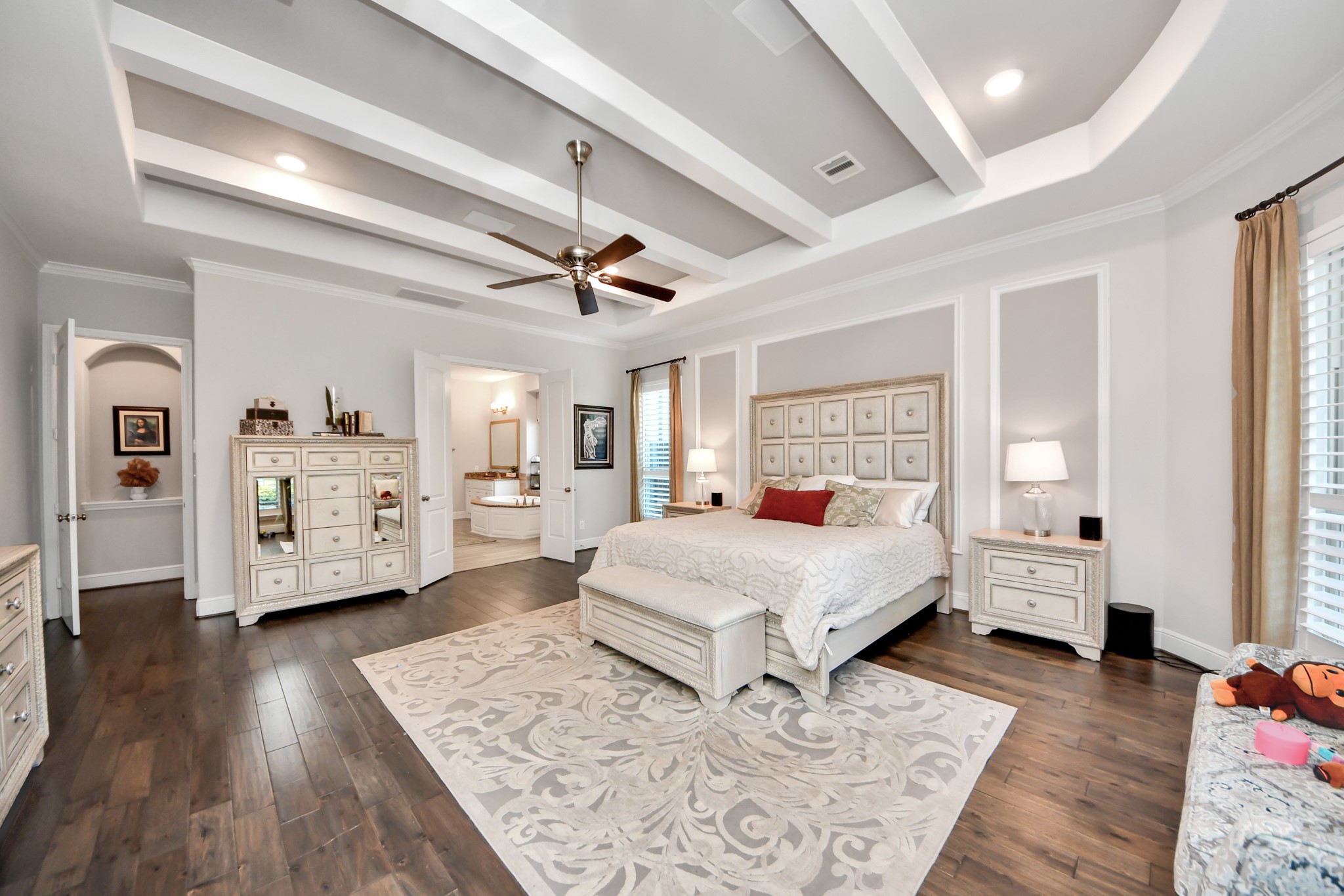 Expansive primary suite featuring rich wood flooring, decorative ceiling beams, built-in surround sound speakers, and a spacious layout.