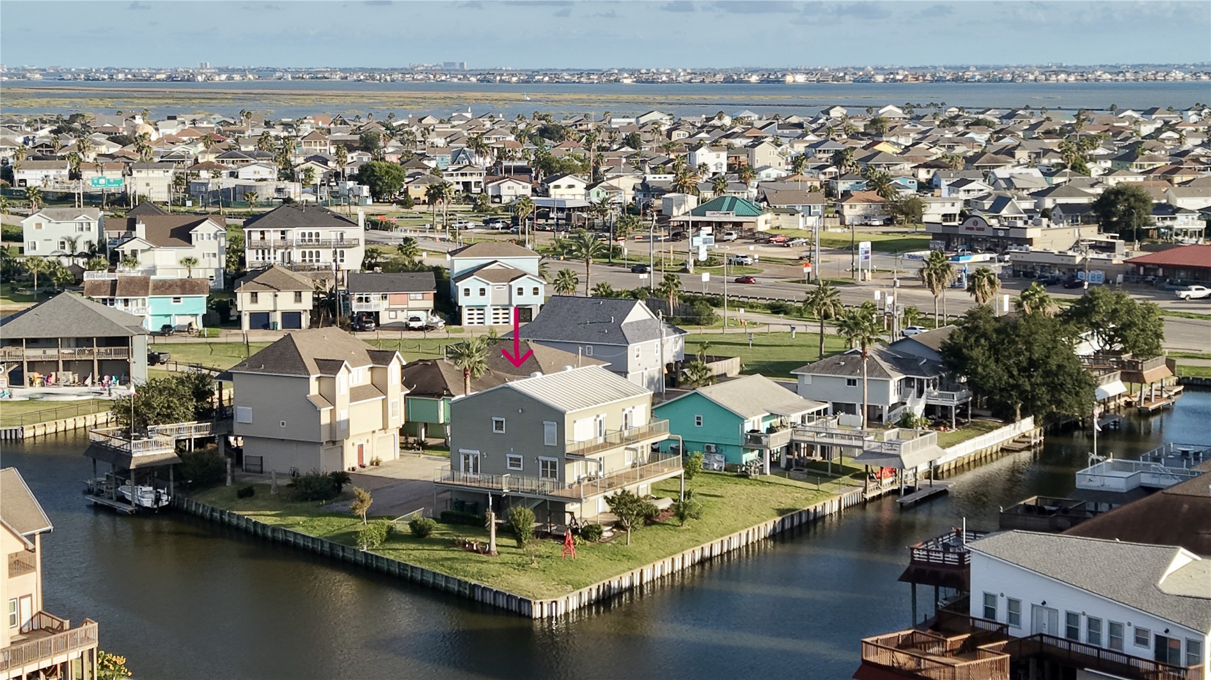 Aerial view of the home on its point lot, with water on two sides and a bulkhead wrapping the property. Across Highway 6 you can see Bayou Vista, and Tiki Island sits on the horizon, a clear picture of how connected this corner of the coast is.