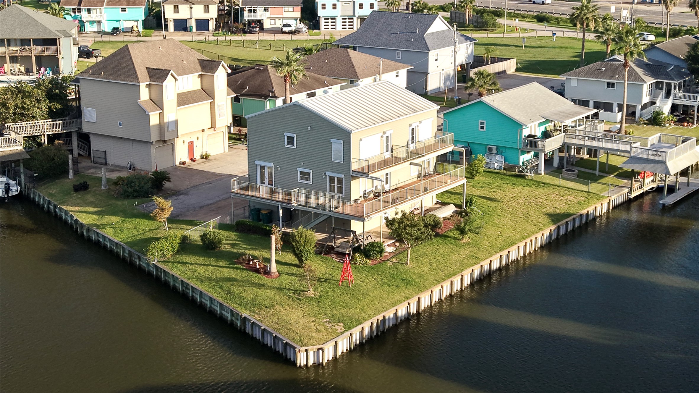 A closer look from the water side: two open-air balconies on the upper level, plus a wraparound deck below that's partly covered for shade. A wide lawn with established landscaping runs right to the new vinyl bulkhead. With two lots, there's room to spread out, entertain, and enjoy the waterfront from almost every angle.