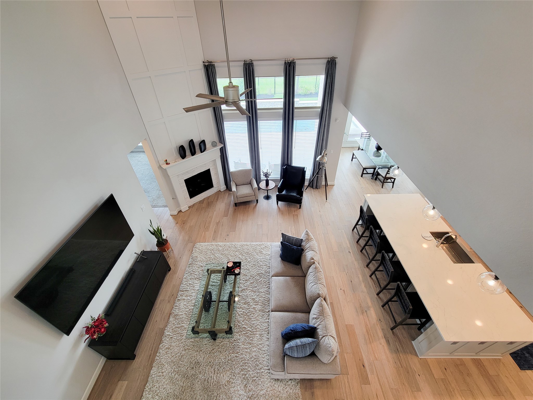 Spacious, open-concept living area with high ceilings, a modern kitchen island, and large windows offering plenty of natural light. The room features a cozy seating area, a wall-mounted TV, and a fireplace. Ideal for entertaining.